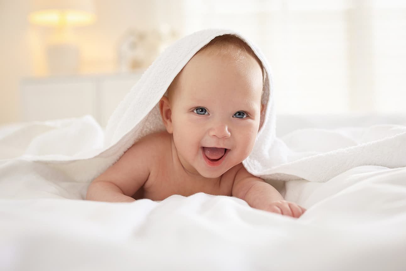 Cute newborn baby wrapped with white towel on bed indoors