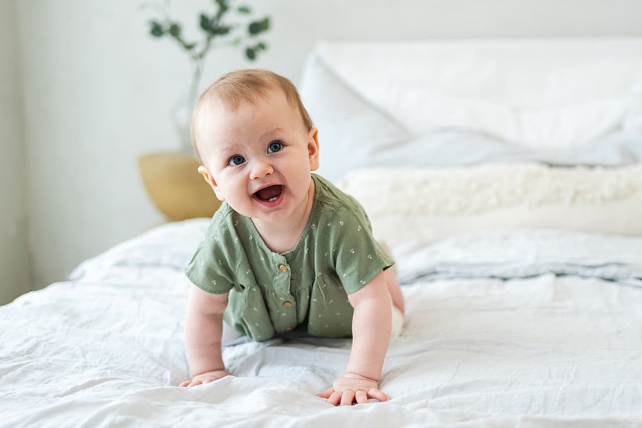 Happy baby. Cute little newborn girl with smiling face crawling on bed in bedroom. Infant baby resting playing lying down on blanket at home. Motherhood happy child childcare concept