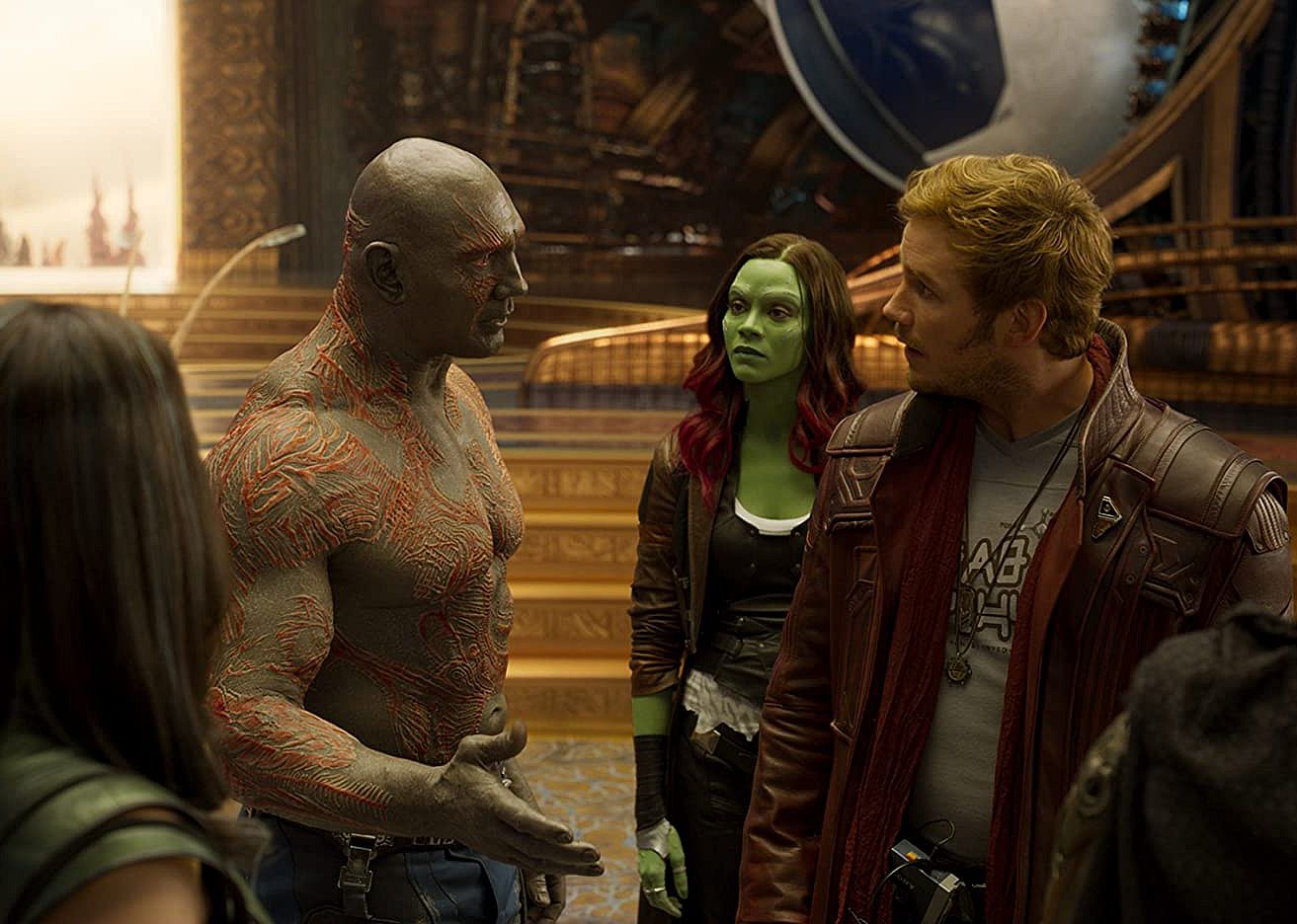 Dave Bautista (with full body scars), Zoe Saldana (as a green being) and Chris Pratt talking.