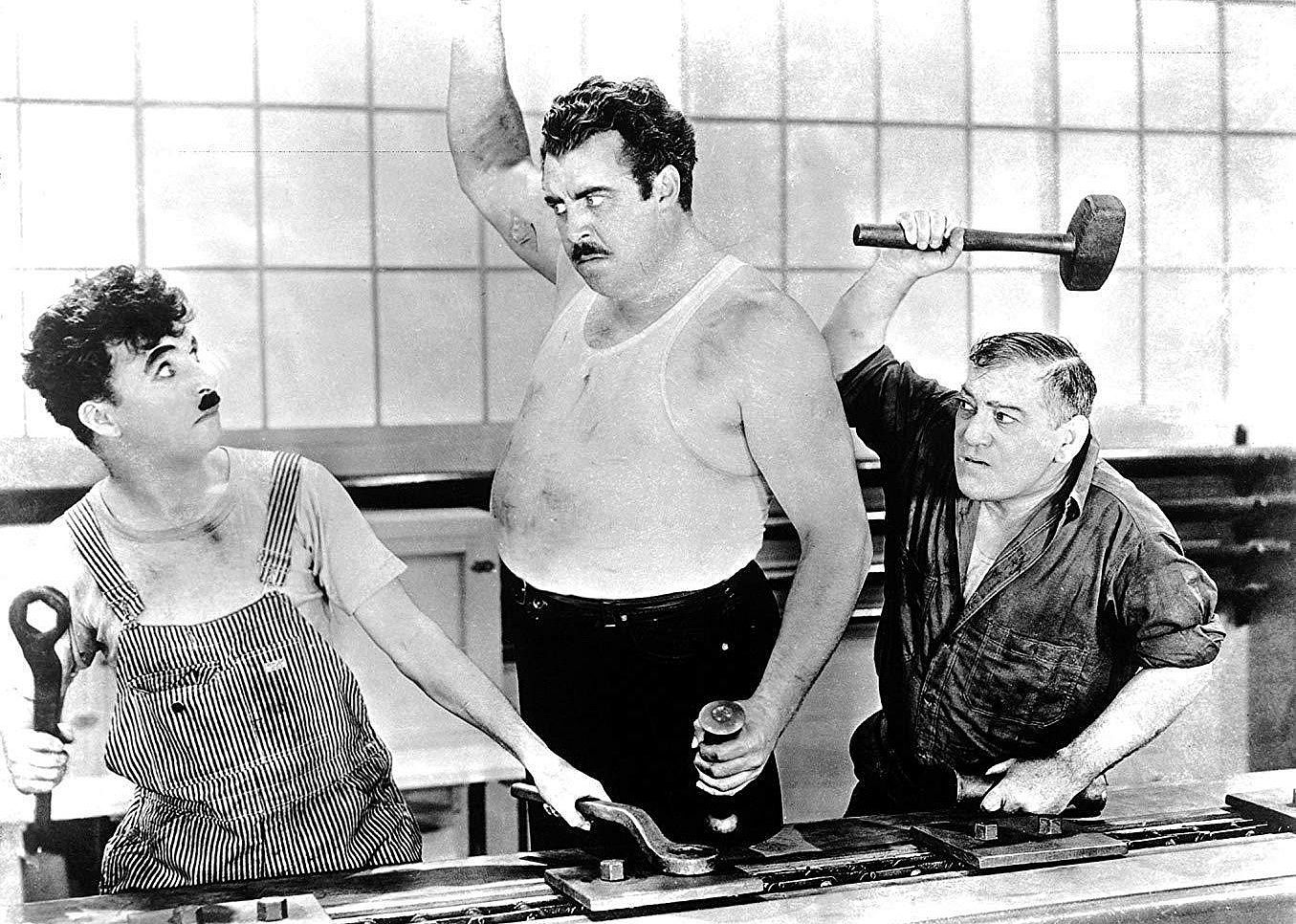 Black and white image of three men holding tools while working in a factory who look angry at each other.