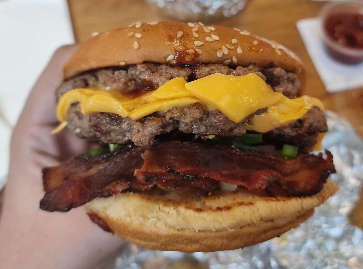A hand holding a Bacon Cheeseburger from Five Guys
