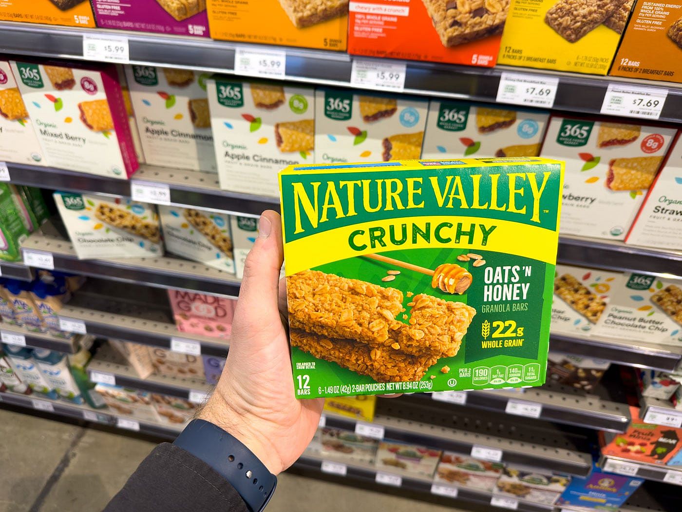 A hand holding a box of Nature Valley Crunchy oats 'n honey bar in the aisle of a Whole Foods
