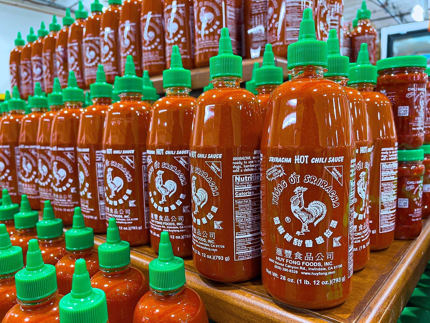 Plastic bottles of Huy Fong Foods Sriracha sauce in a supermarket aisle.