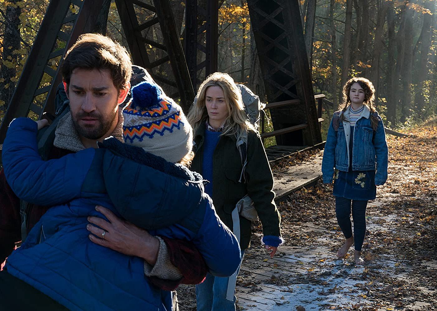 John Krasinski and Emily Blunt walk across a bridge with two kids.