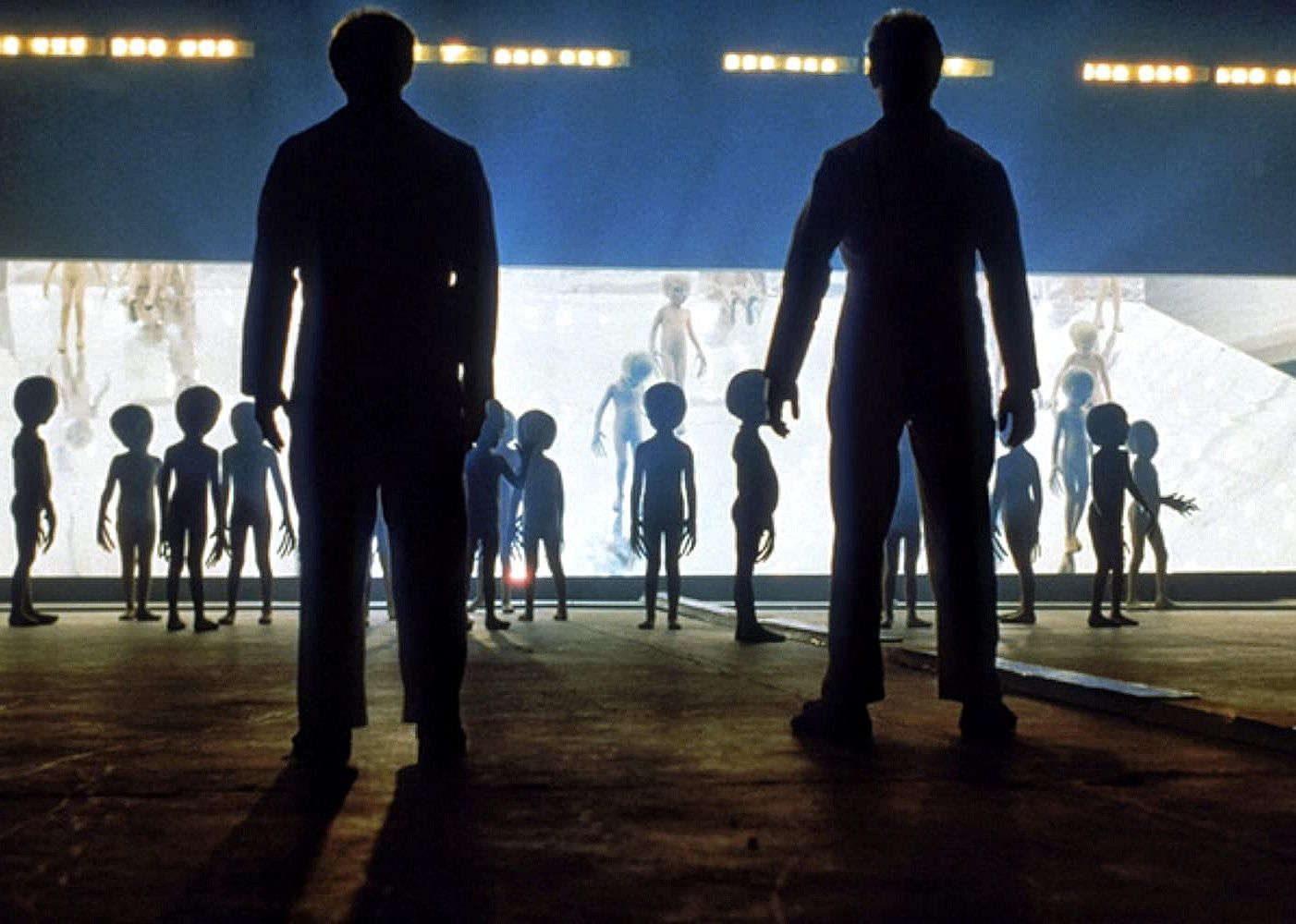 Two men standing at the opening of a space ship with small beings all around.