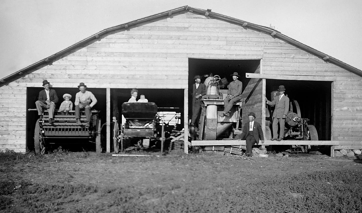 Various family members and farm hands sit on the equipment parked in the barn for a portrait circa 1910.