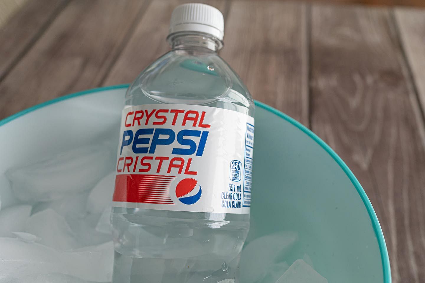 A bottle of Crystal Pepsi sitting in a bowl of ice.