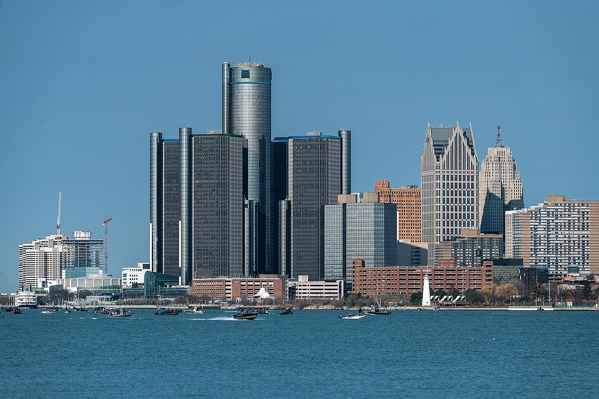 View of the Detroit skyline from across the Detroit River, featuring the Renaissance Center and surrounding high-rise buildings on a clear spring day.