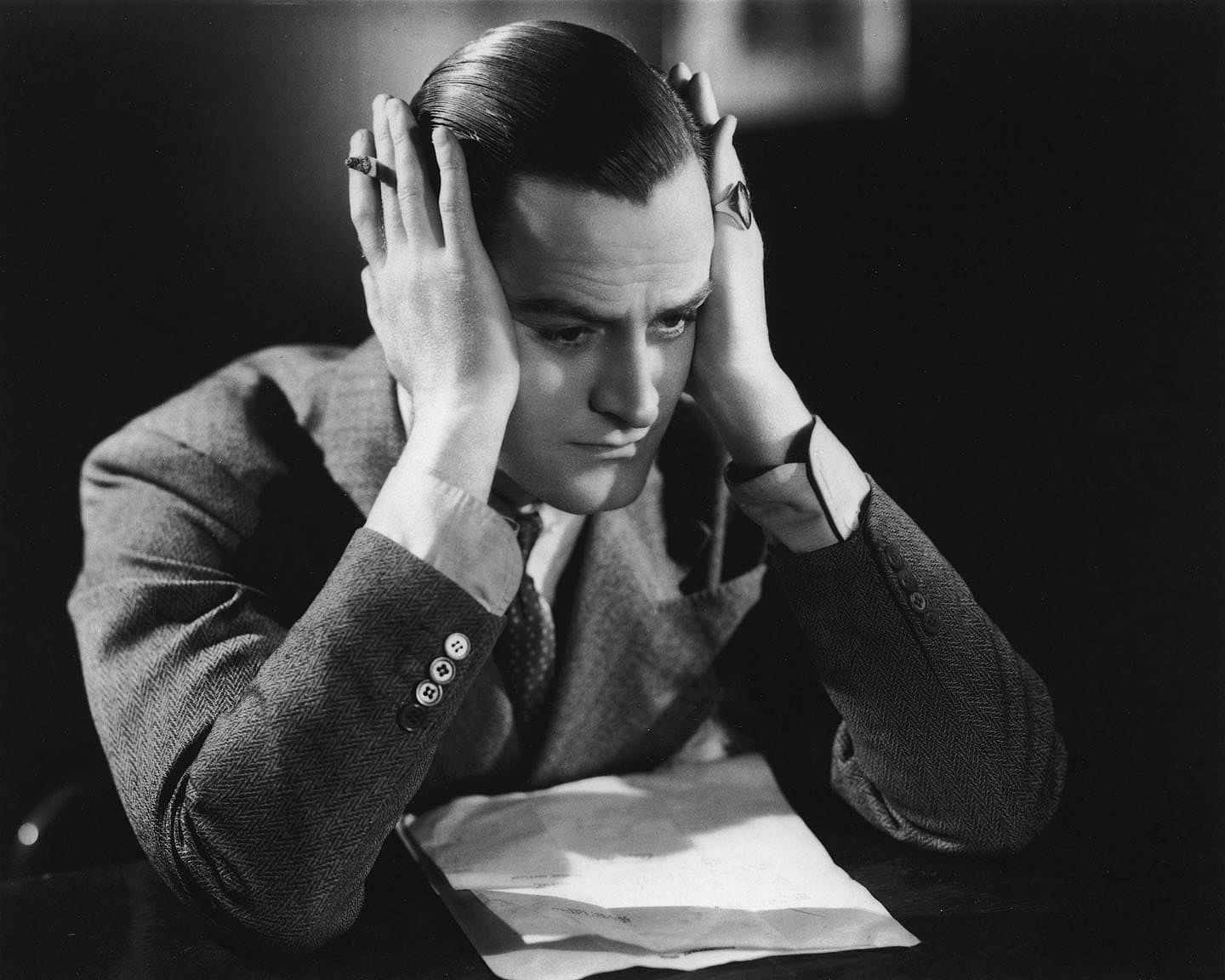 A man resting his head in his hands as he contemplates a letter on the desk in front of him, circa 1935.