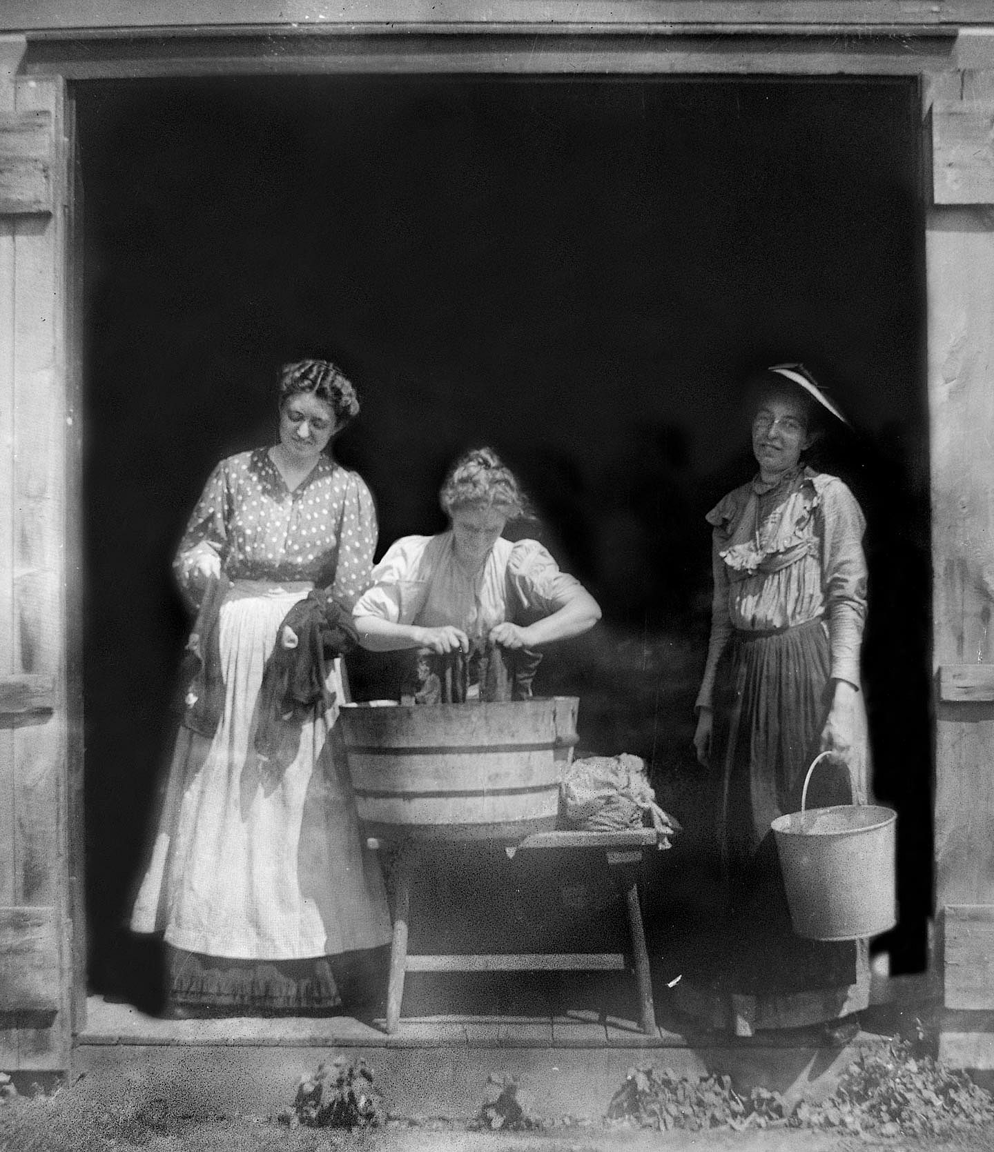 Three women in 1915 washing clothing in front of a barn