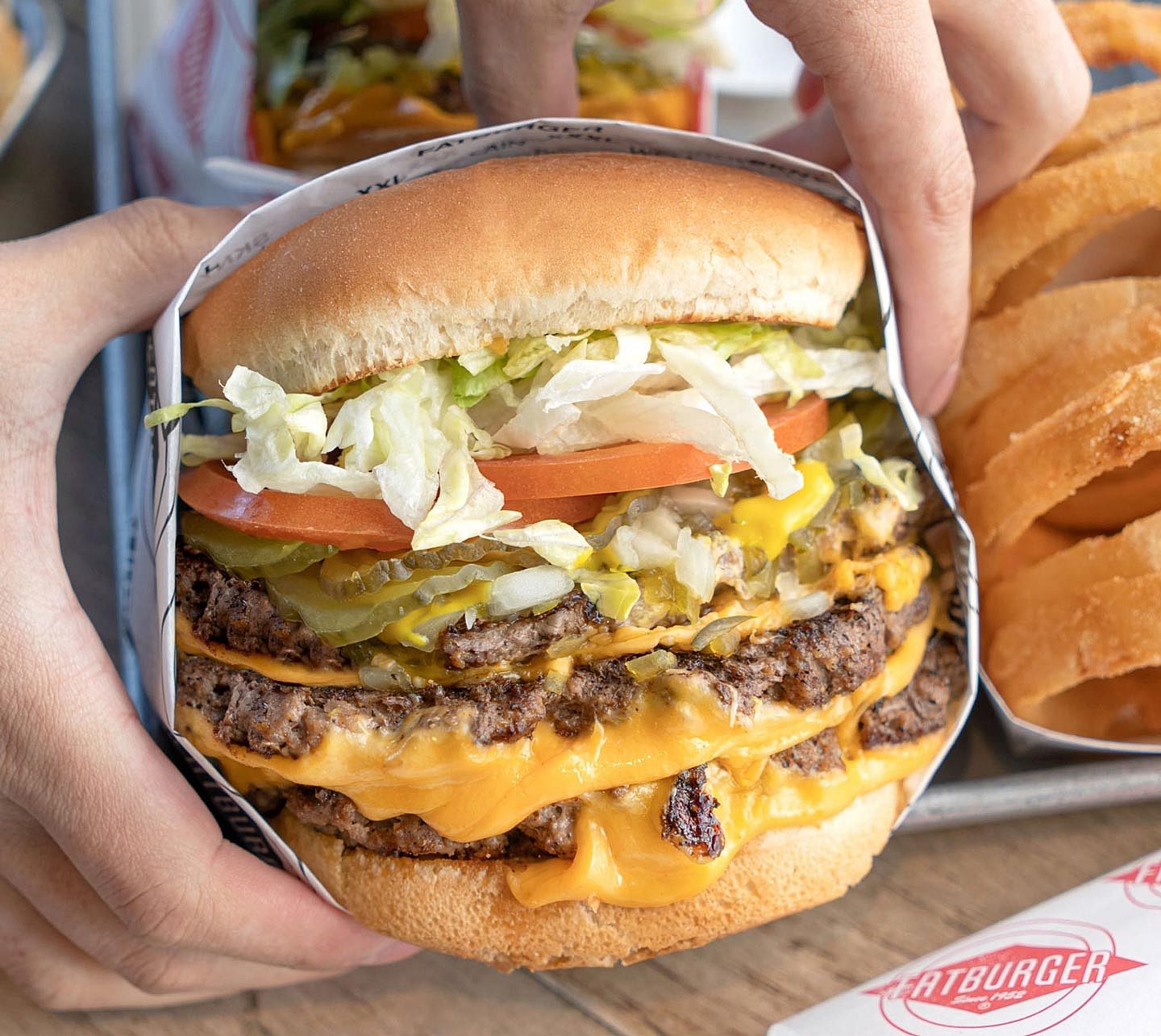 Hands holding an XXXL Triple Kingburger from Fatburger