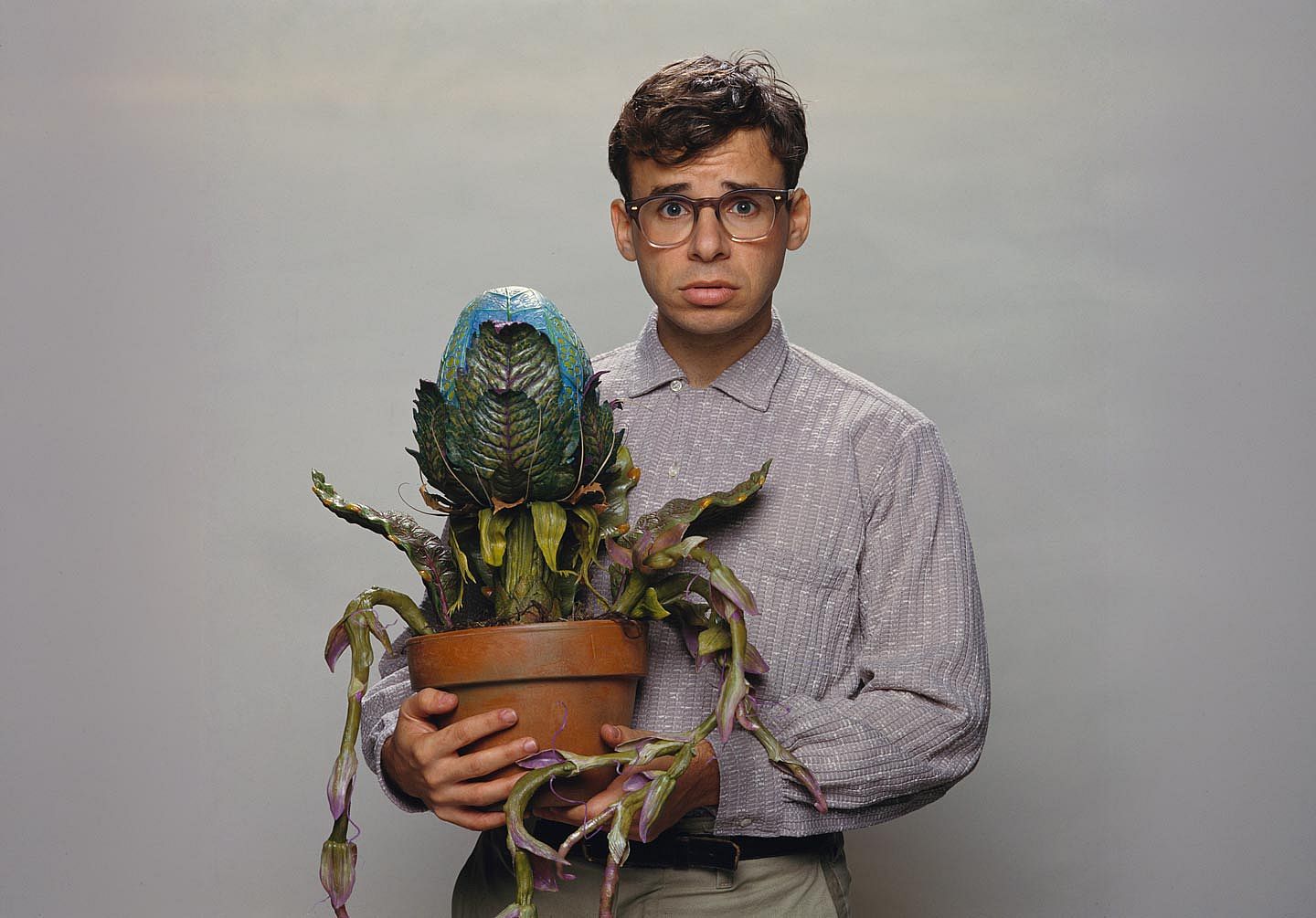 Rick Moranis holding a monster plant while looking afraid during Little Shop of Horrors (1986)