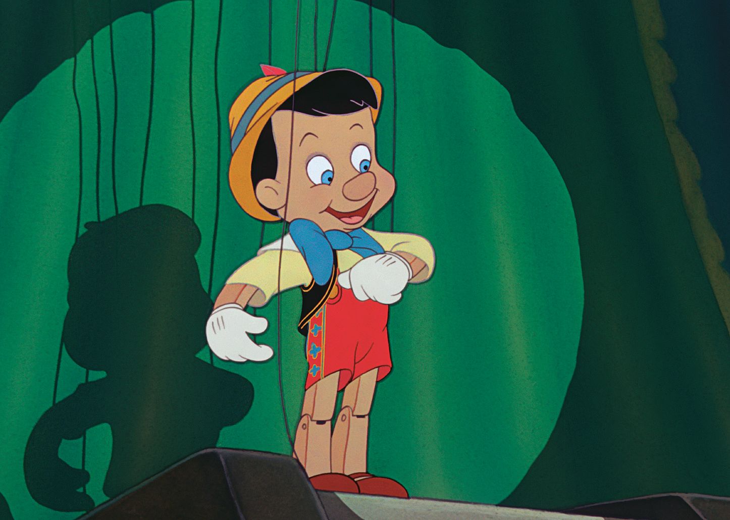 A cartoon of a Pinocchio, a puppet who is a little boy, onstage in front of a green curtain.