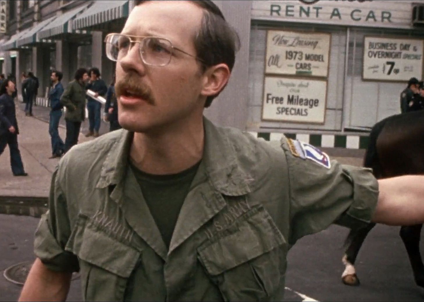 A man in an army uniform standing on the street talking to people.
