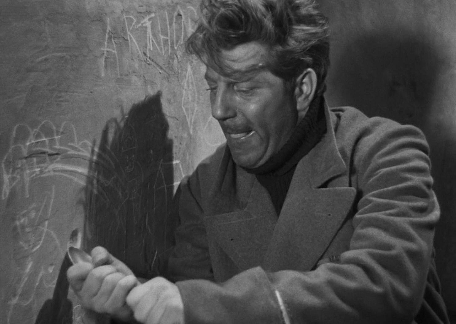 A man trapped in a room using a spoon to carve on the wall.