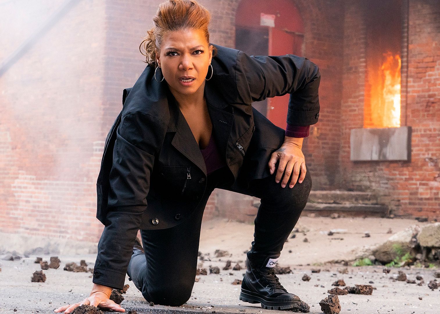 A woman kneels down facing away from a burning building.