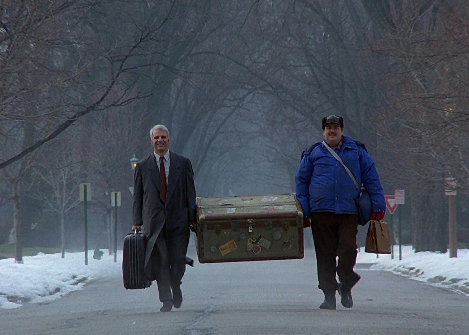 Steve Martin and John Candy carrying a huge trunk down the road in the snow.
