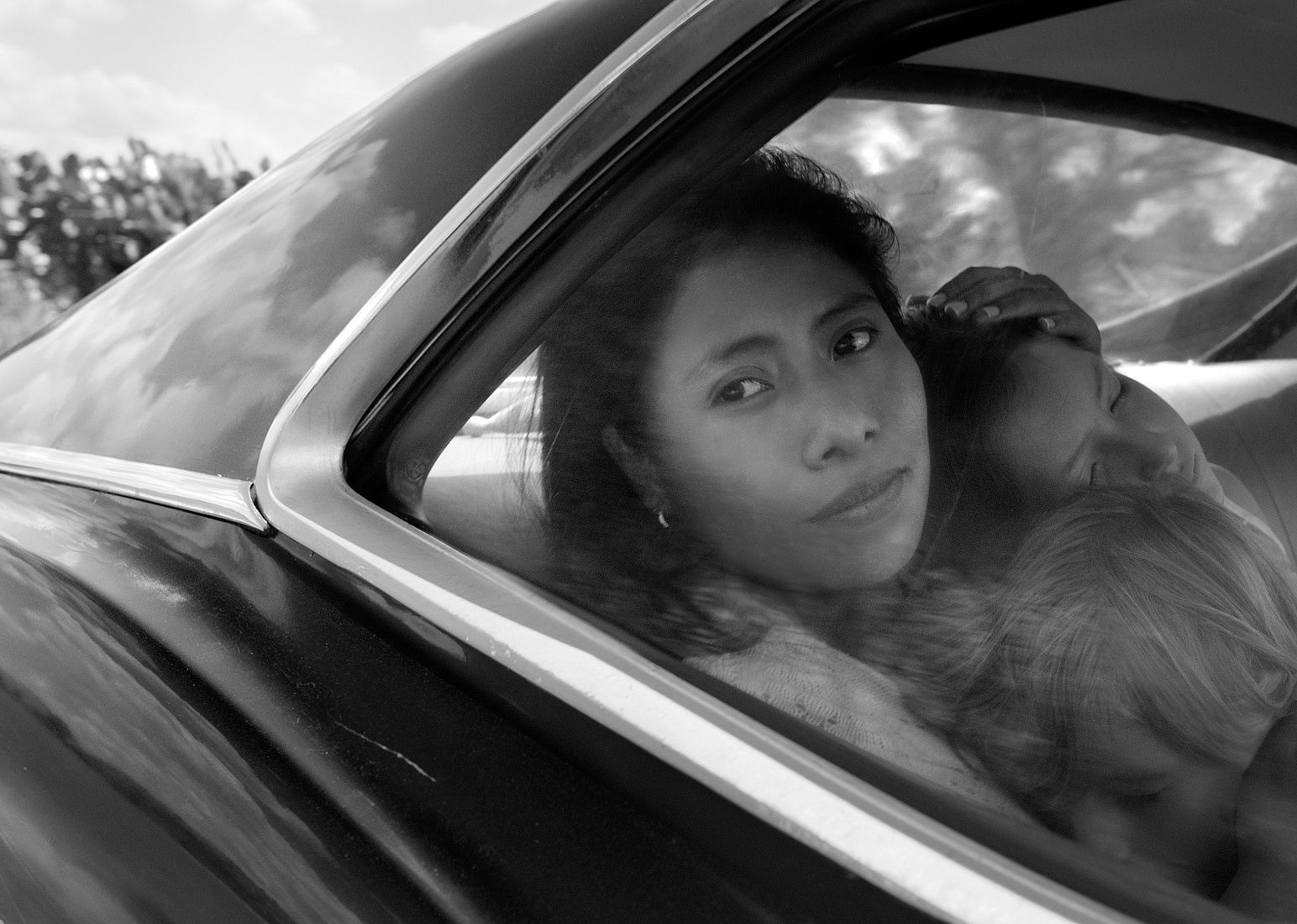 A woman holding two kids in the back seat of a car.