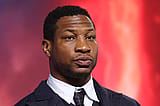 Jonathan Majors in a black suit onstage.
