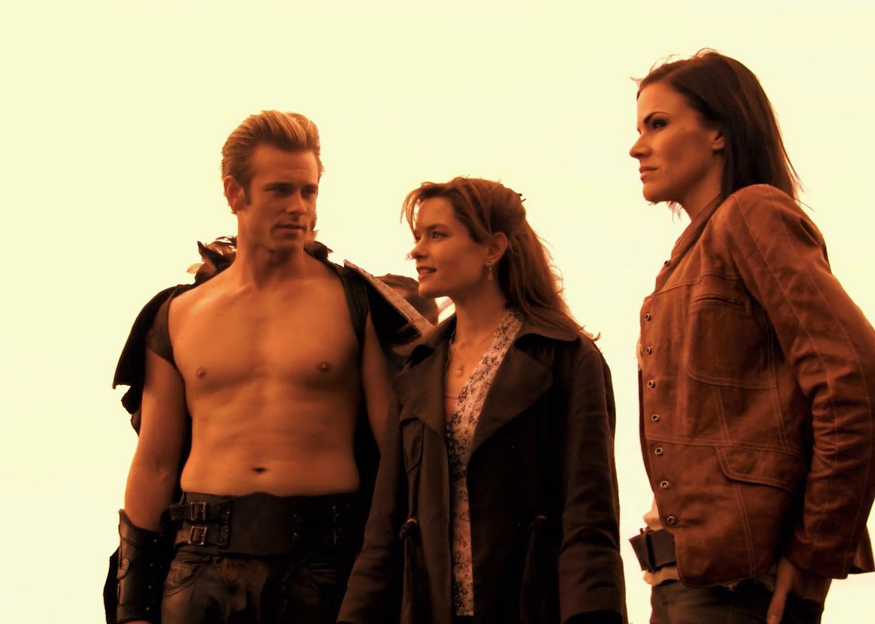 A man with no shirt and a cape talks to two women in regular clothing.