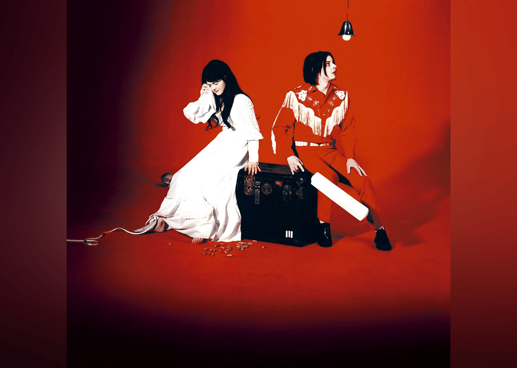 Jack and Meg White in red and white costumes sitting on a trunk.