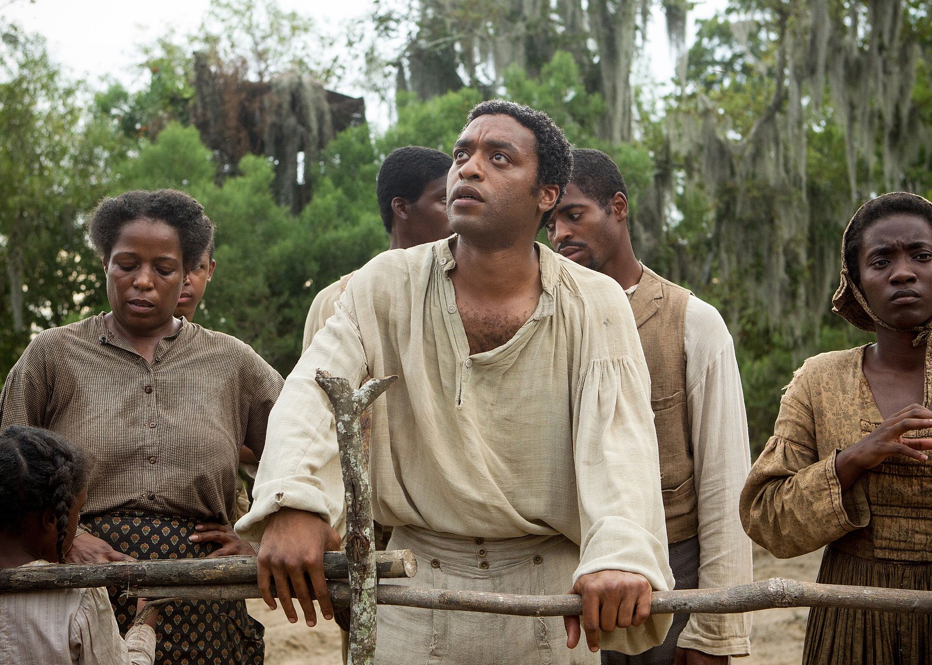 A group of black people standing behind a fence, one man looking up.
