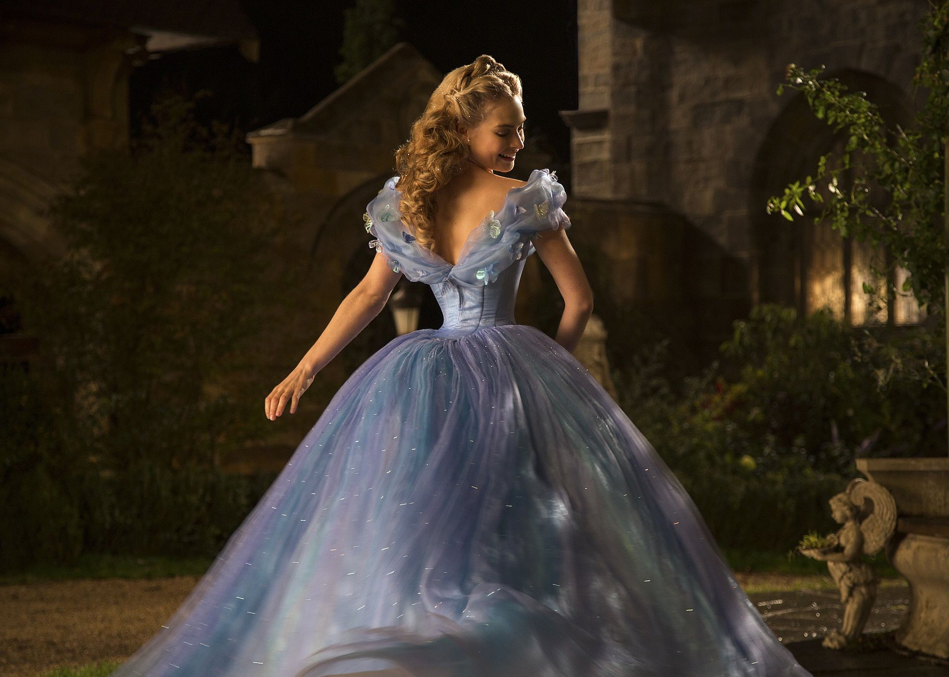 Lily James as Cinderella twirling around in a blue ballgown in a courtyard.