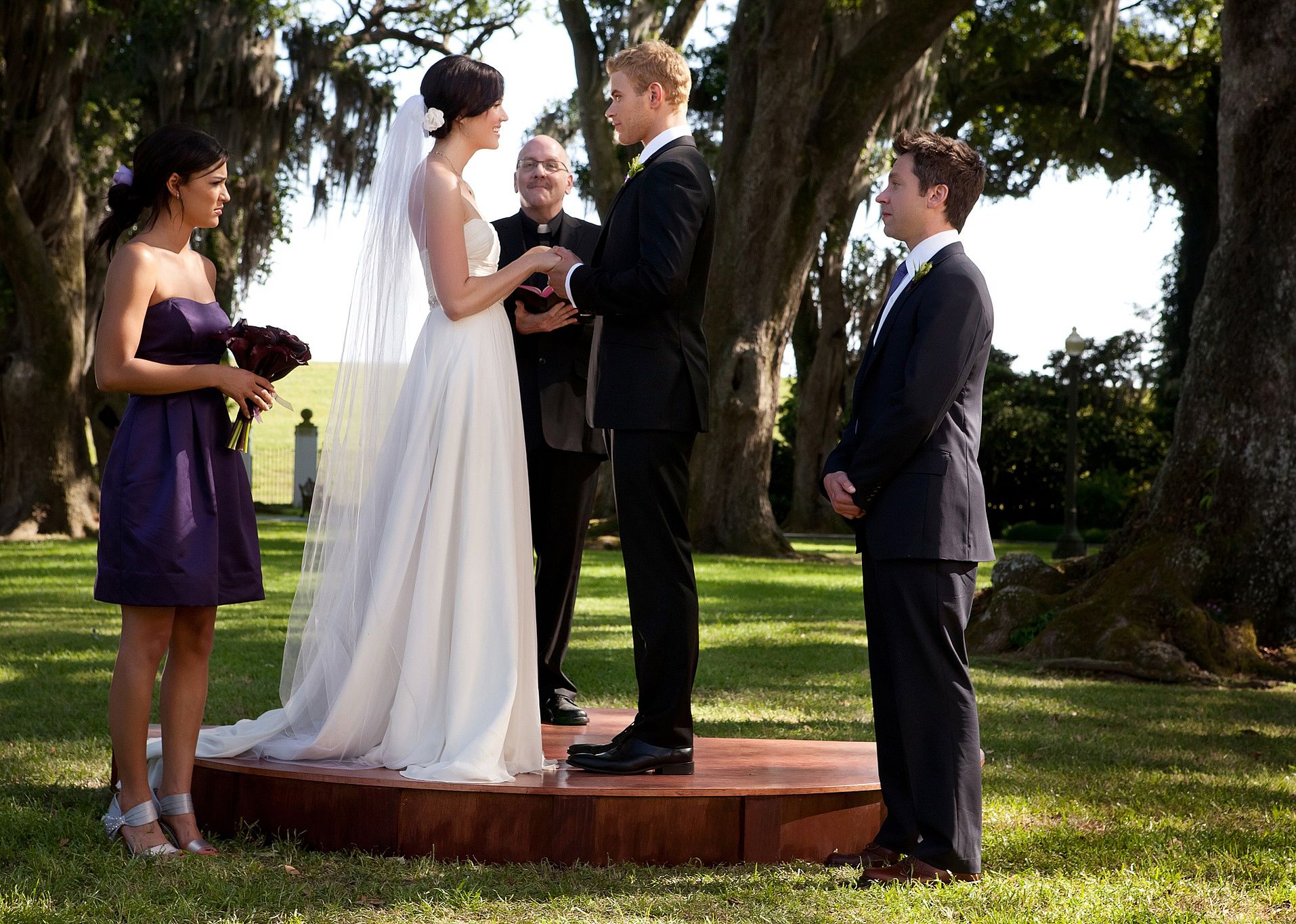 Mandy Moore getting married to a handsome man with one bridesmaid and one groomsman outside.
