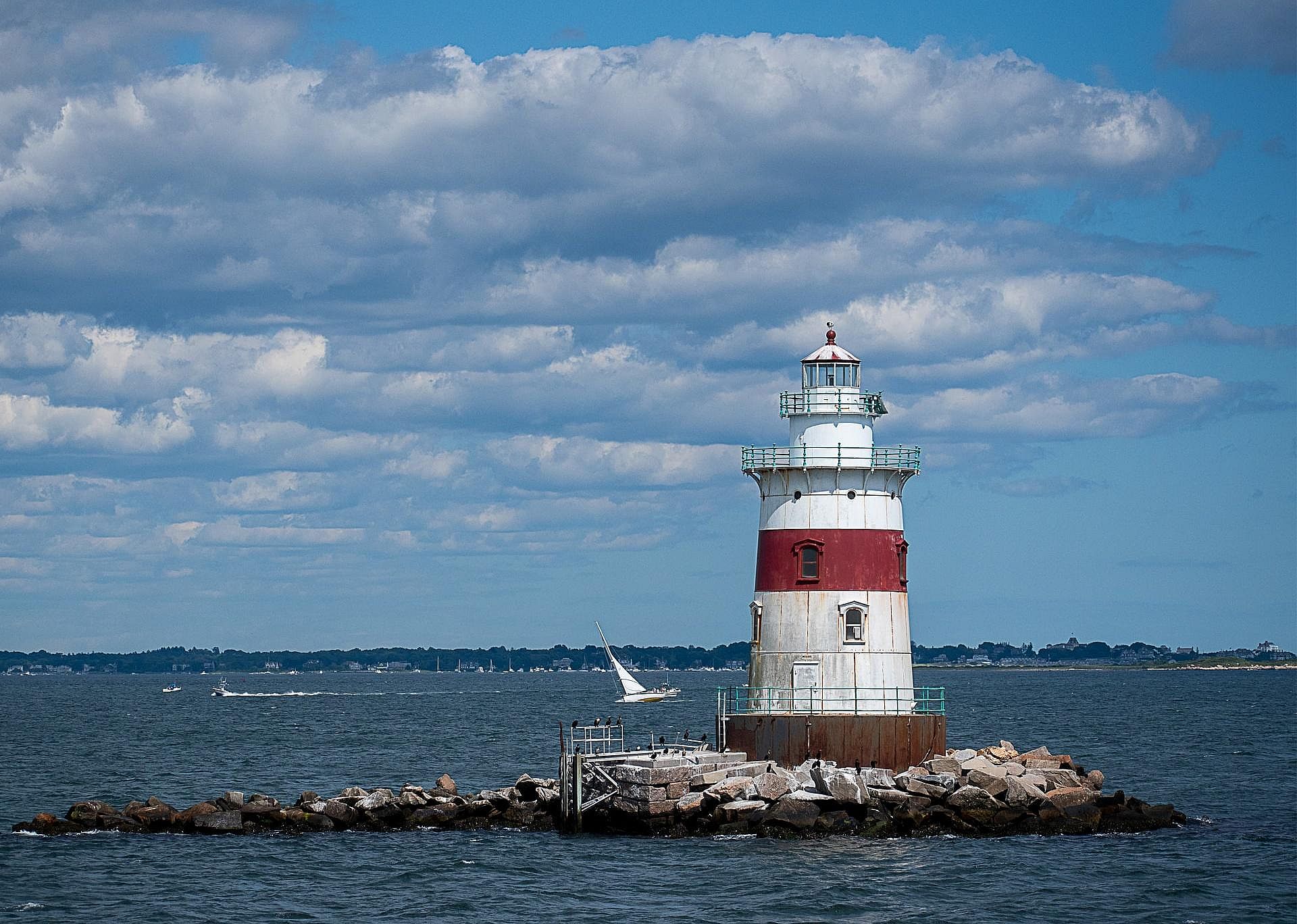 A red and white lighthouse on a small rocky island. 