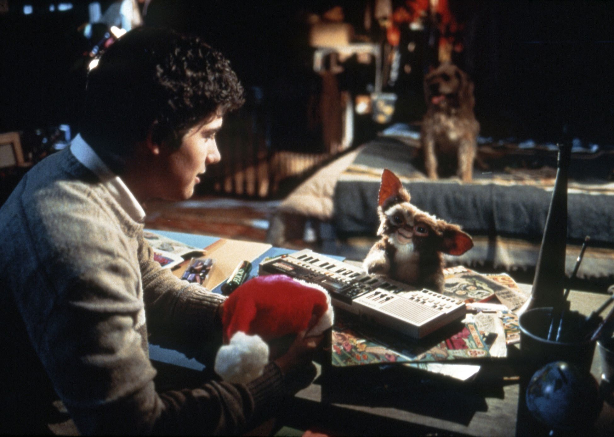 A guy holding a Santa hat while looking at a creature playing a keyboard.