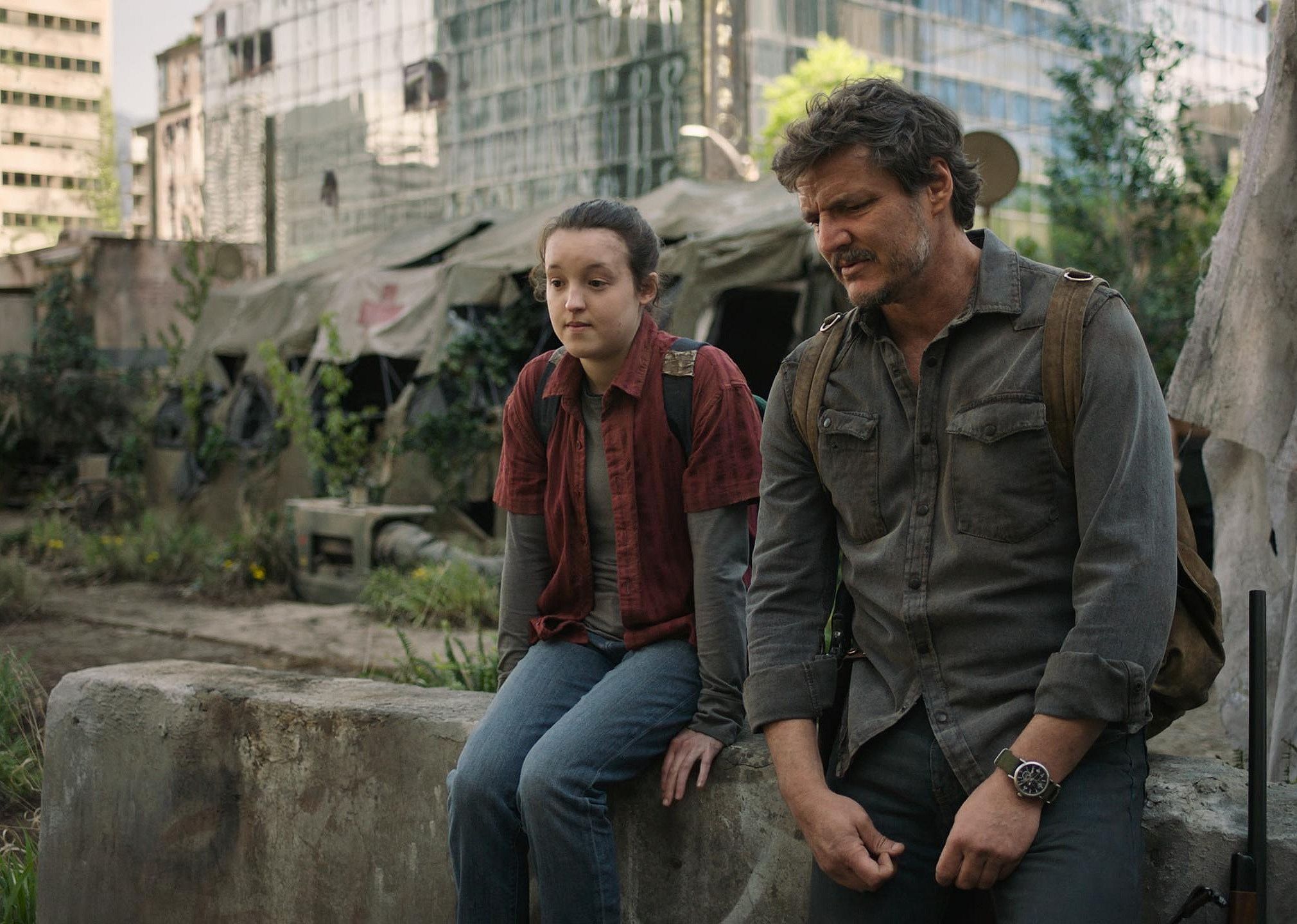 Pedro Pascal and Bella Ramsey in a city in ruins, overgrown with trees and plants. 