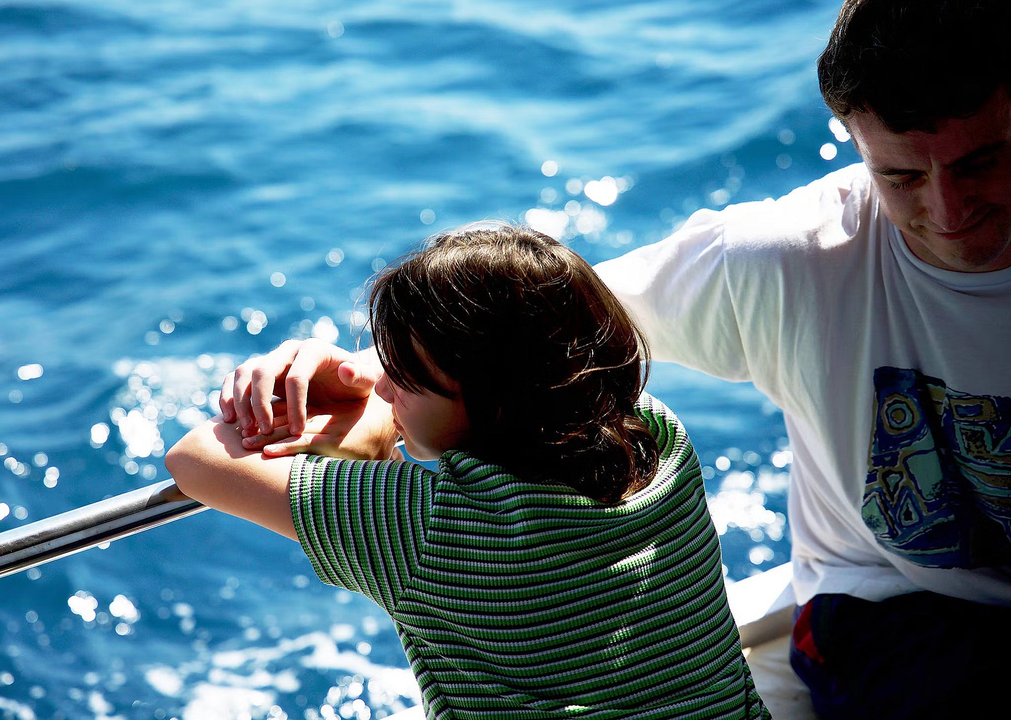 A father and daughter holding hands in the sun on a boat.