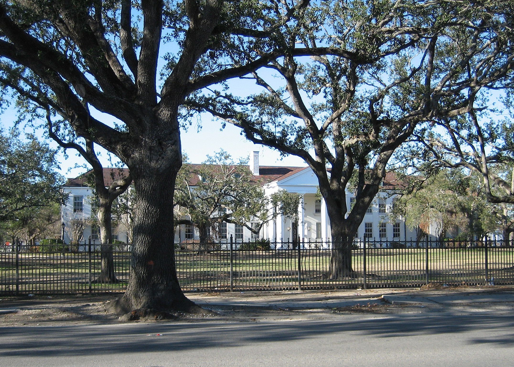 A large historic white building with an iron fence around the perimiter.