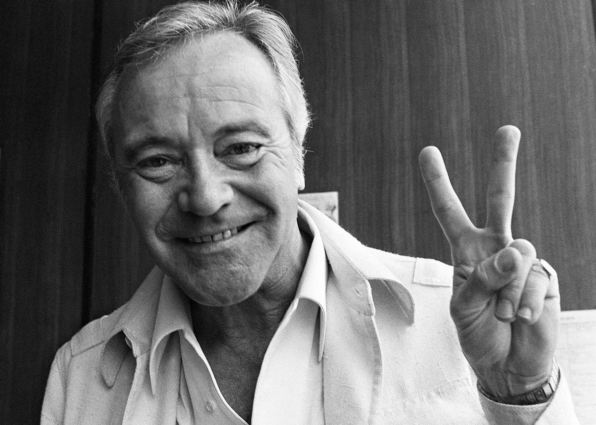 Jack Lemmon smiling, giving the peace sign. 