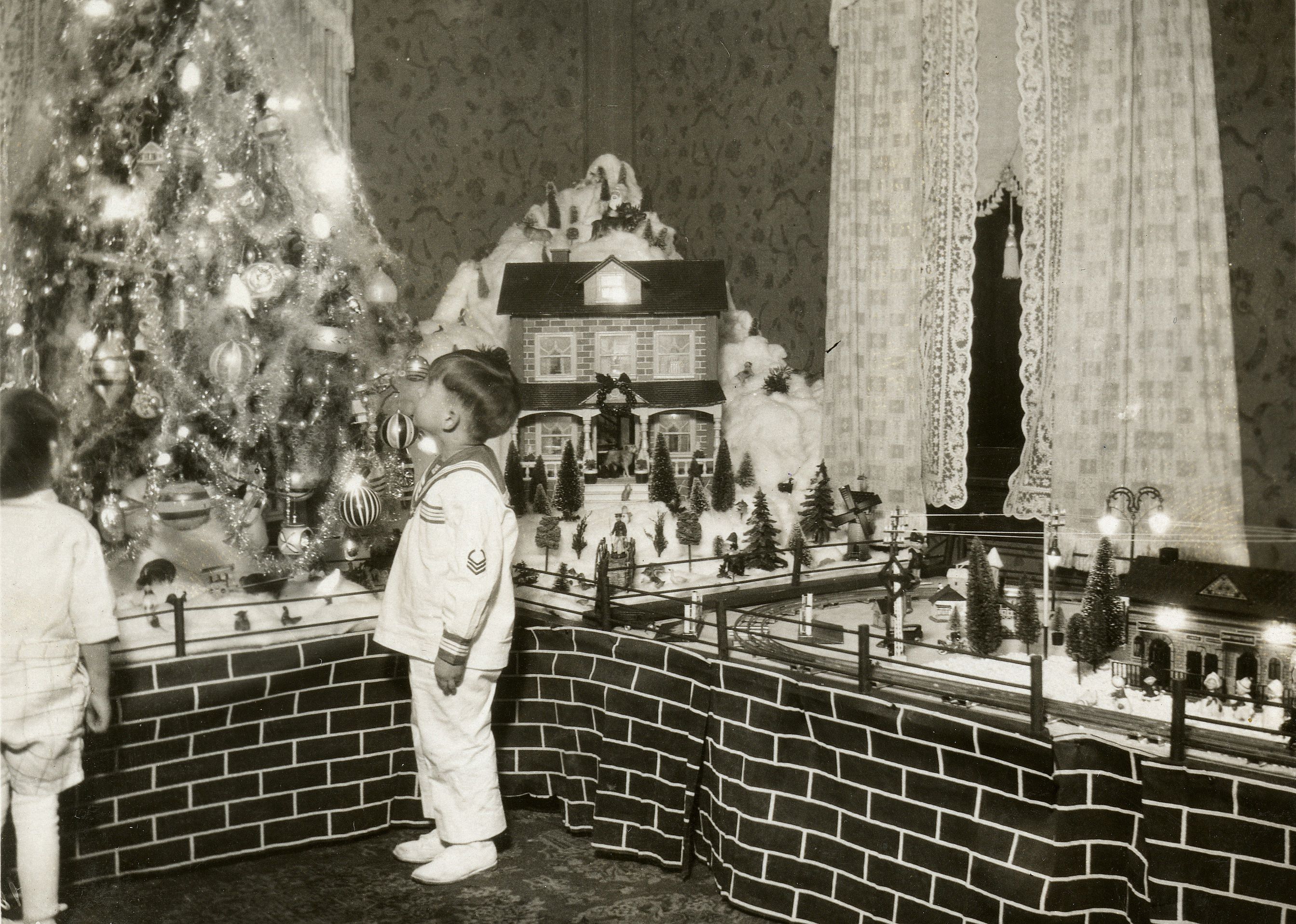 A boy looks up at a Christmas tree decorated with lights.