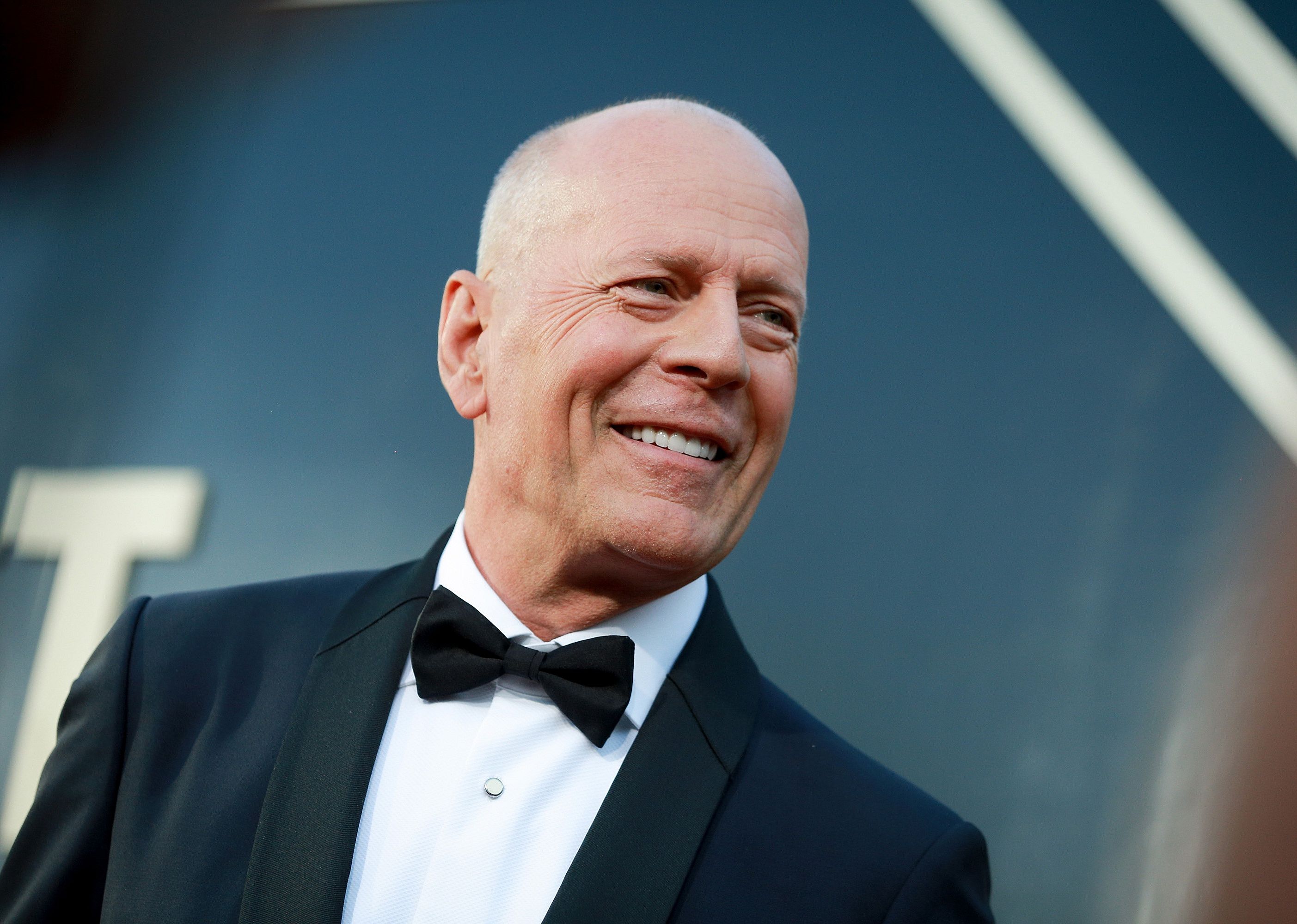 Bruce Willis in a black suit and bowtie.