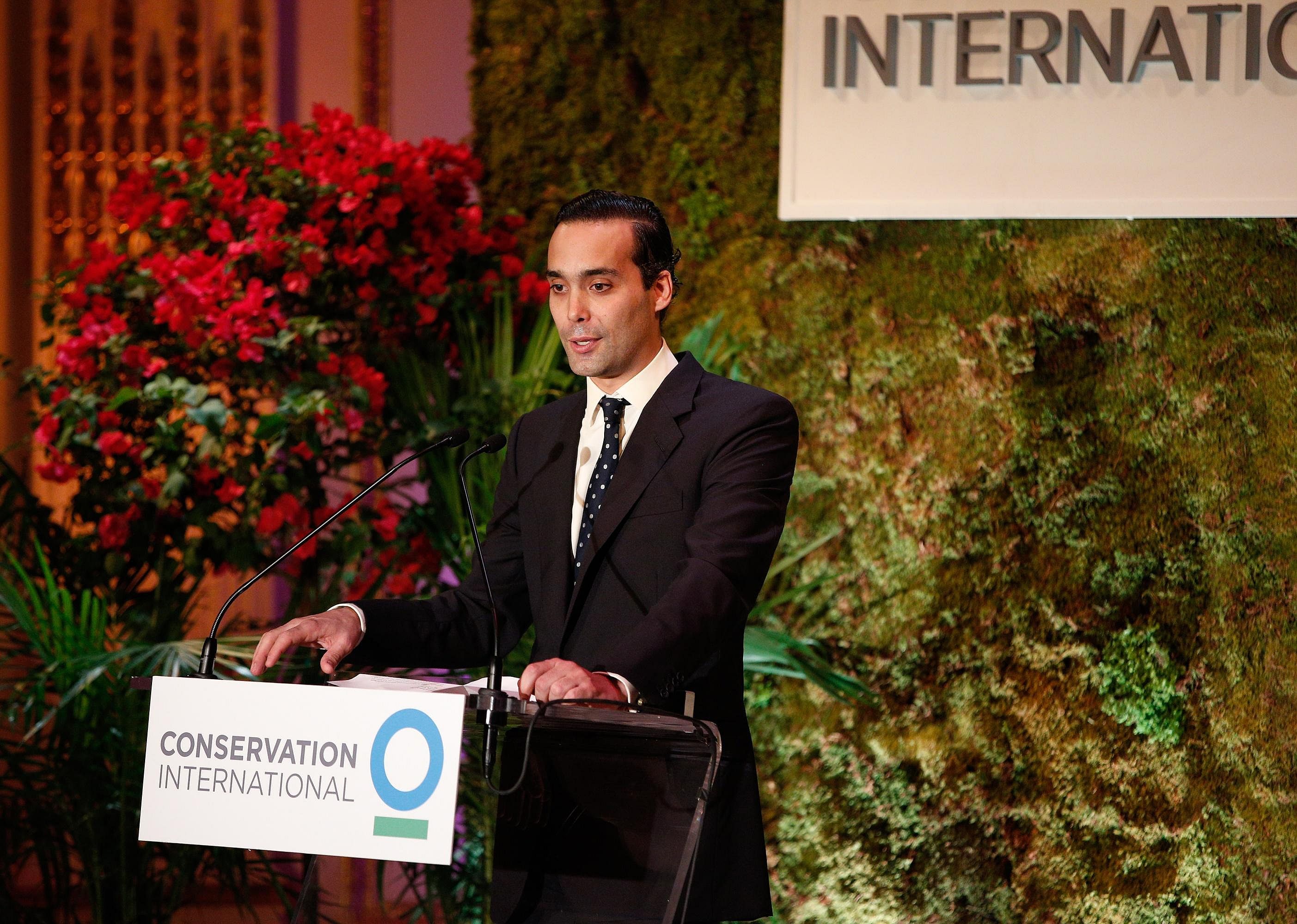 Andres Santo Domingo at a podium in a black suit.