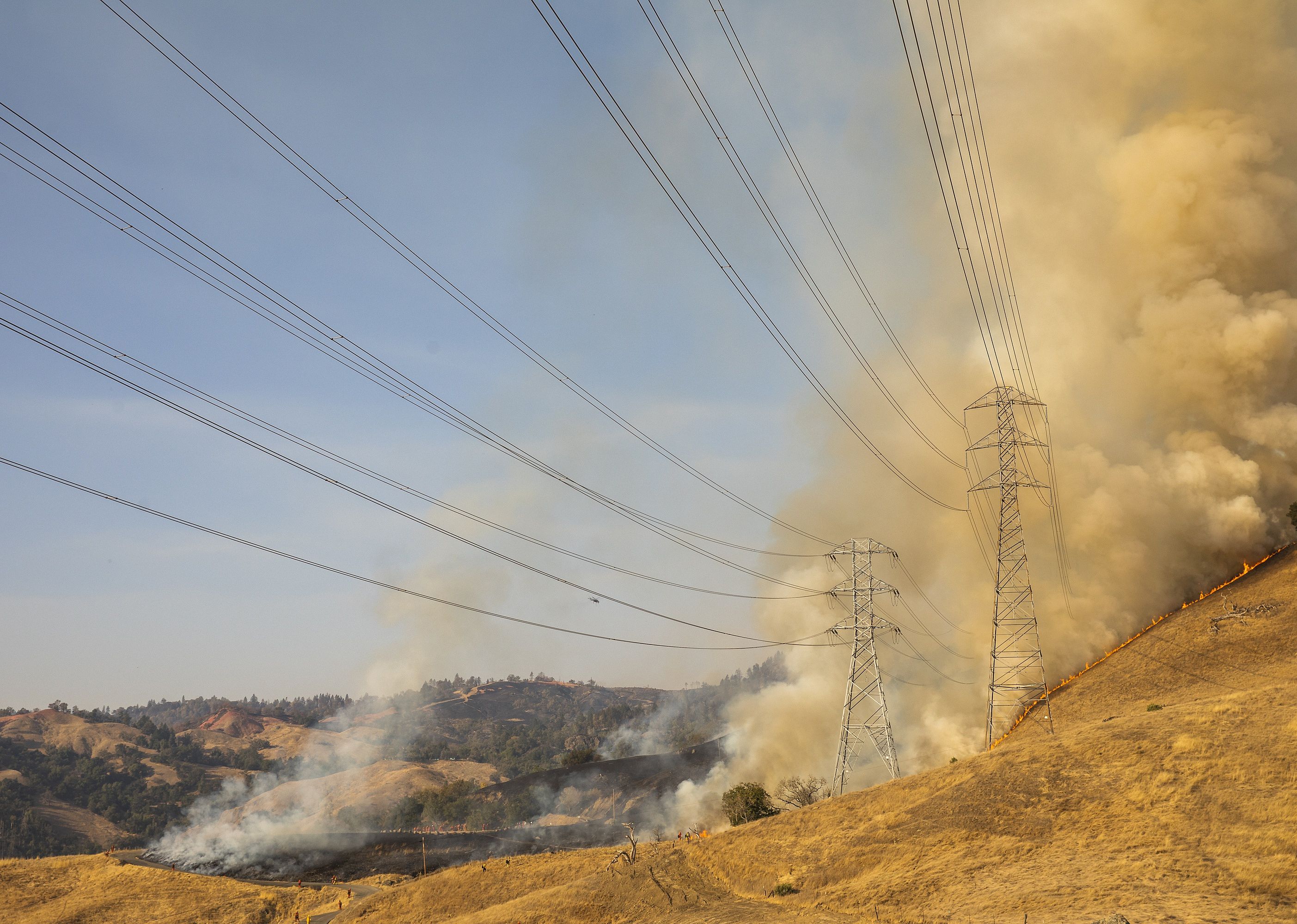 A fire burns a hillside behind PG&E power lines.