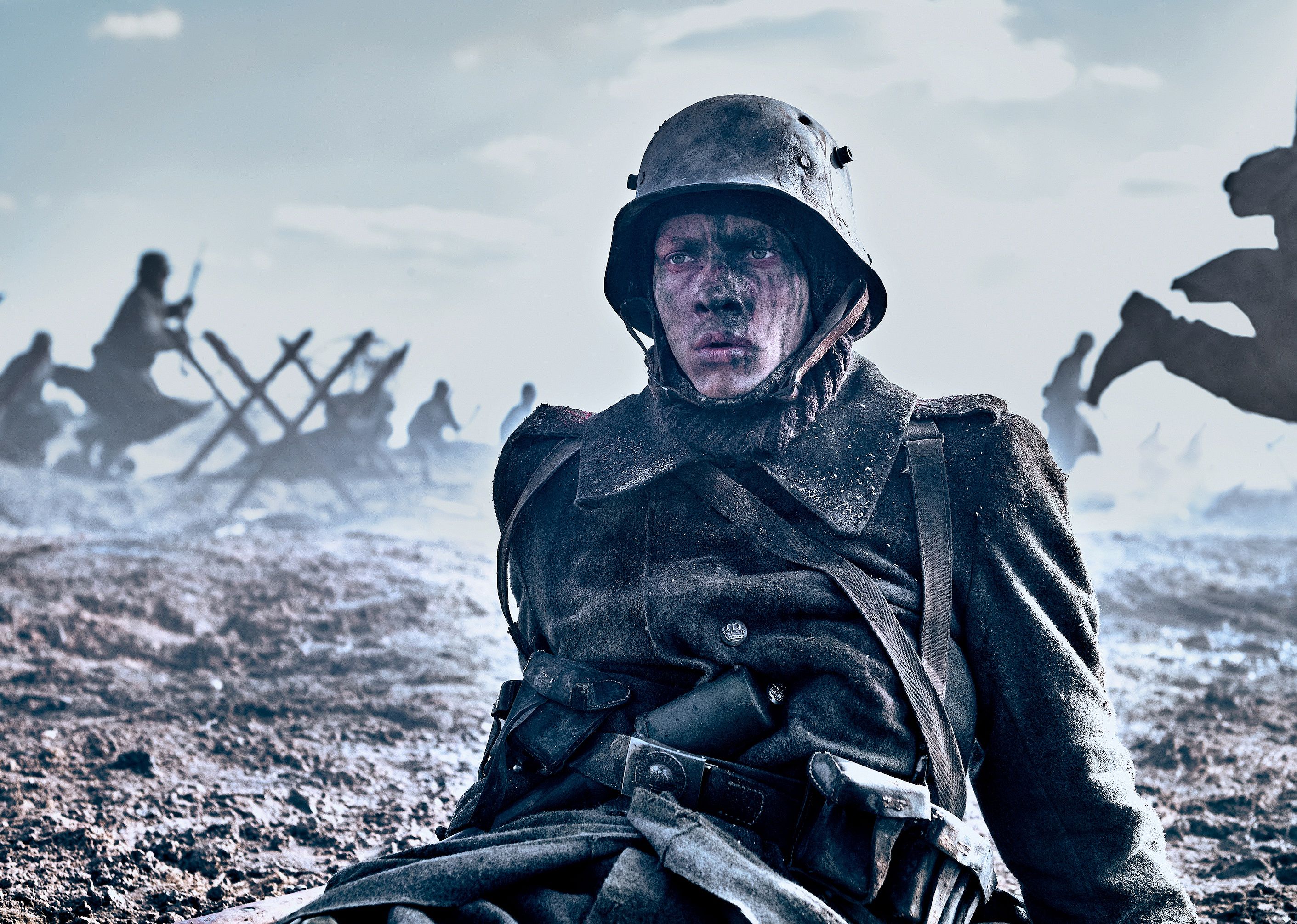 A man battered from battle sits on the ground as chaos ensues around him.