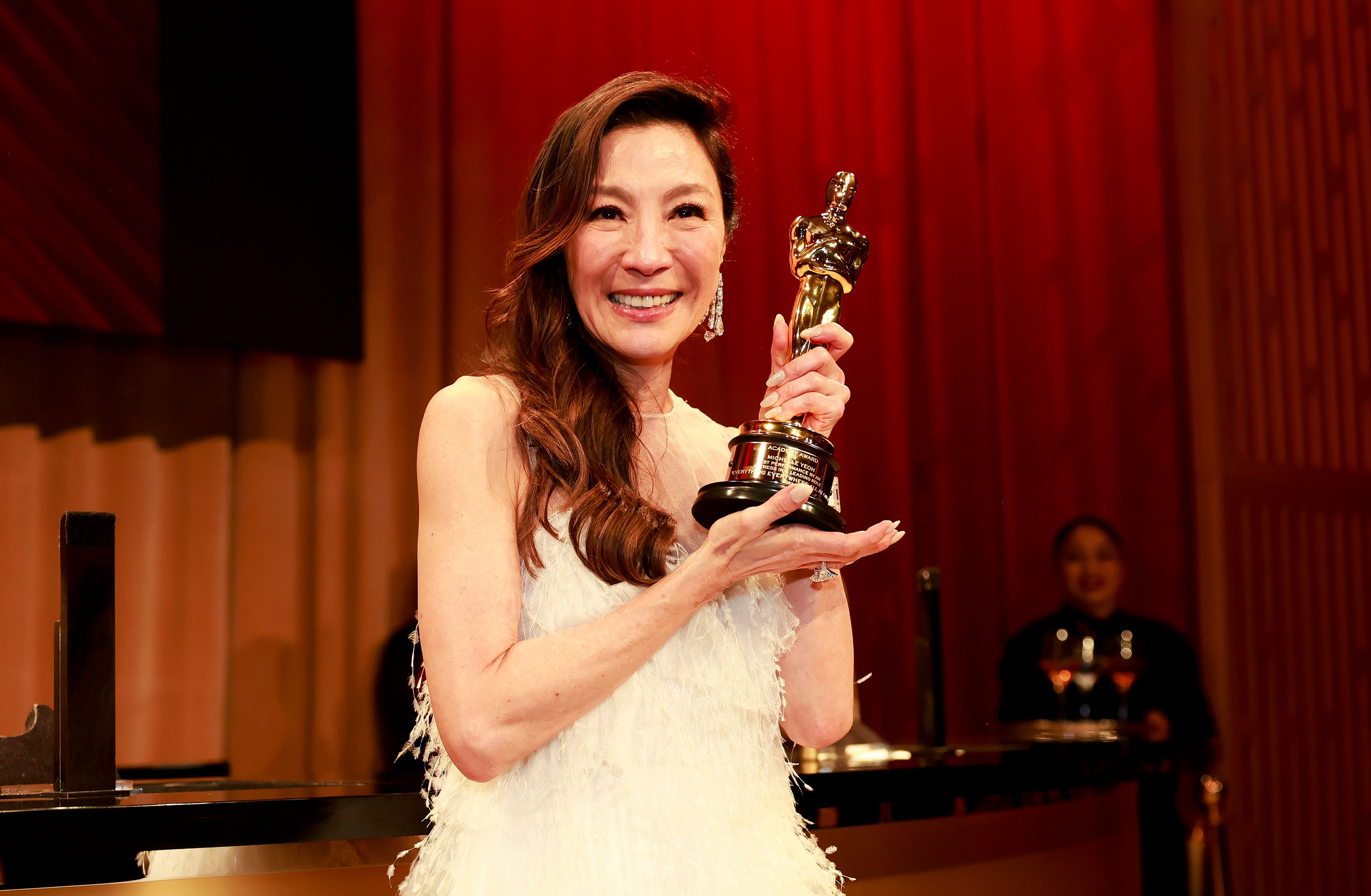 Michelle Yeoh in a white strapless feather gown posing with an Academy Award.