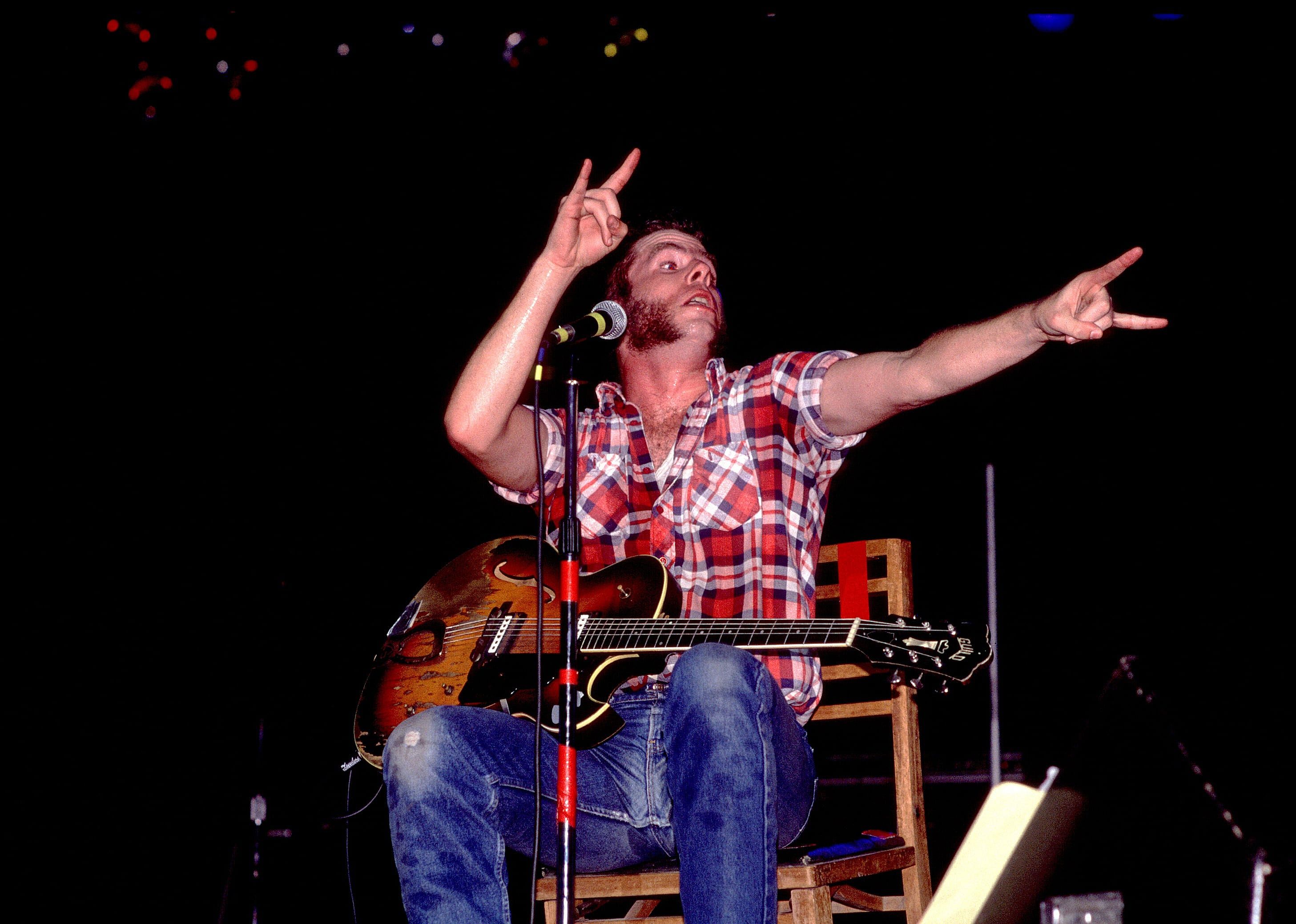 Mojo Nixon seated performing onstage