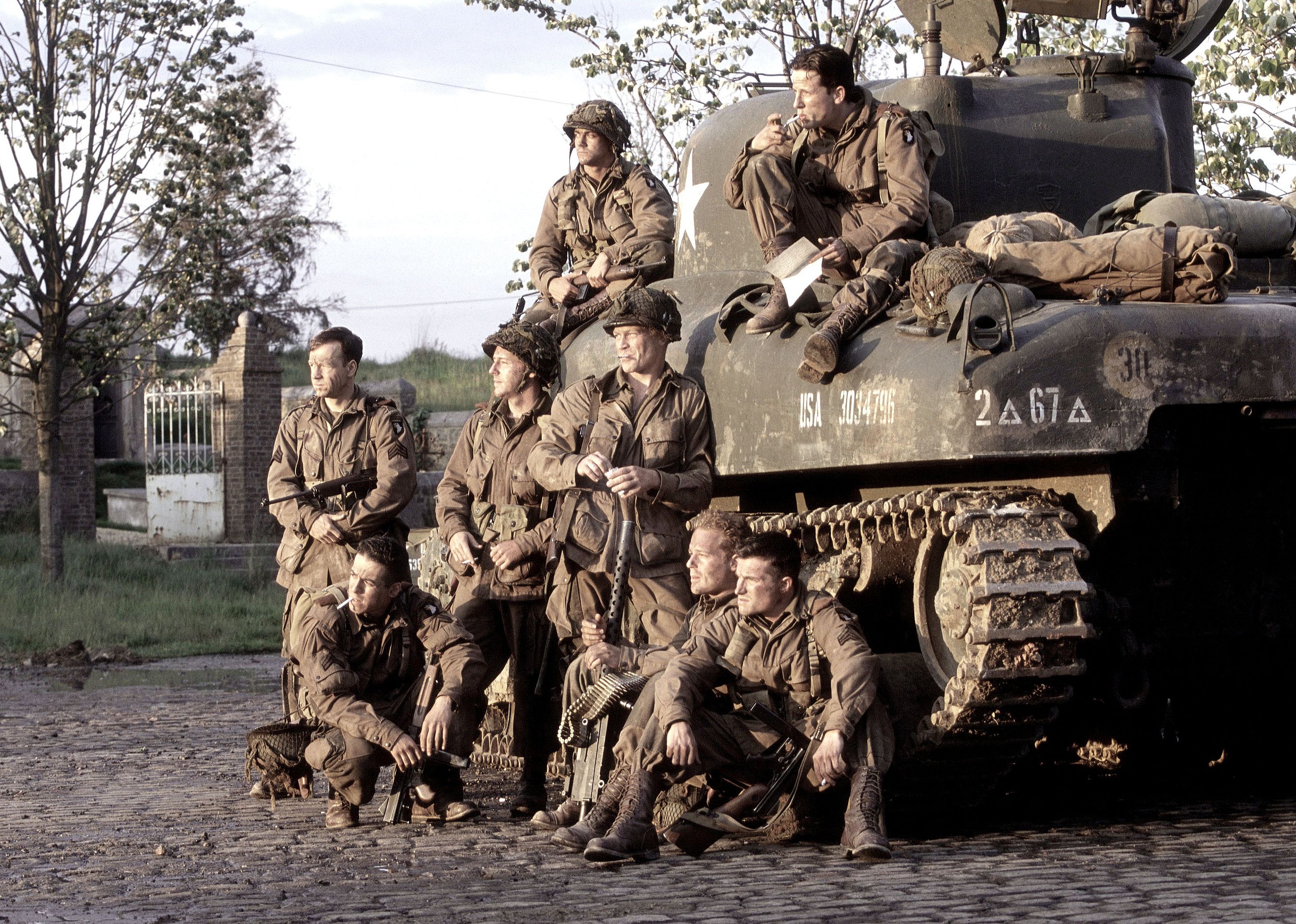 Soldiers seated next to and on top of a tank.