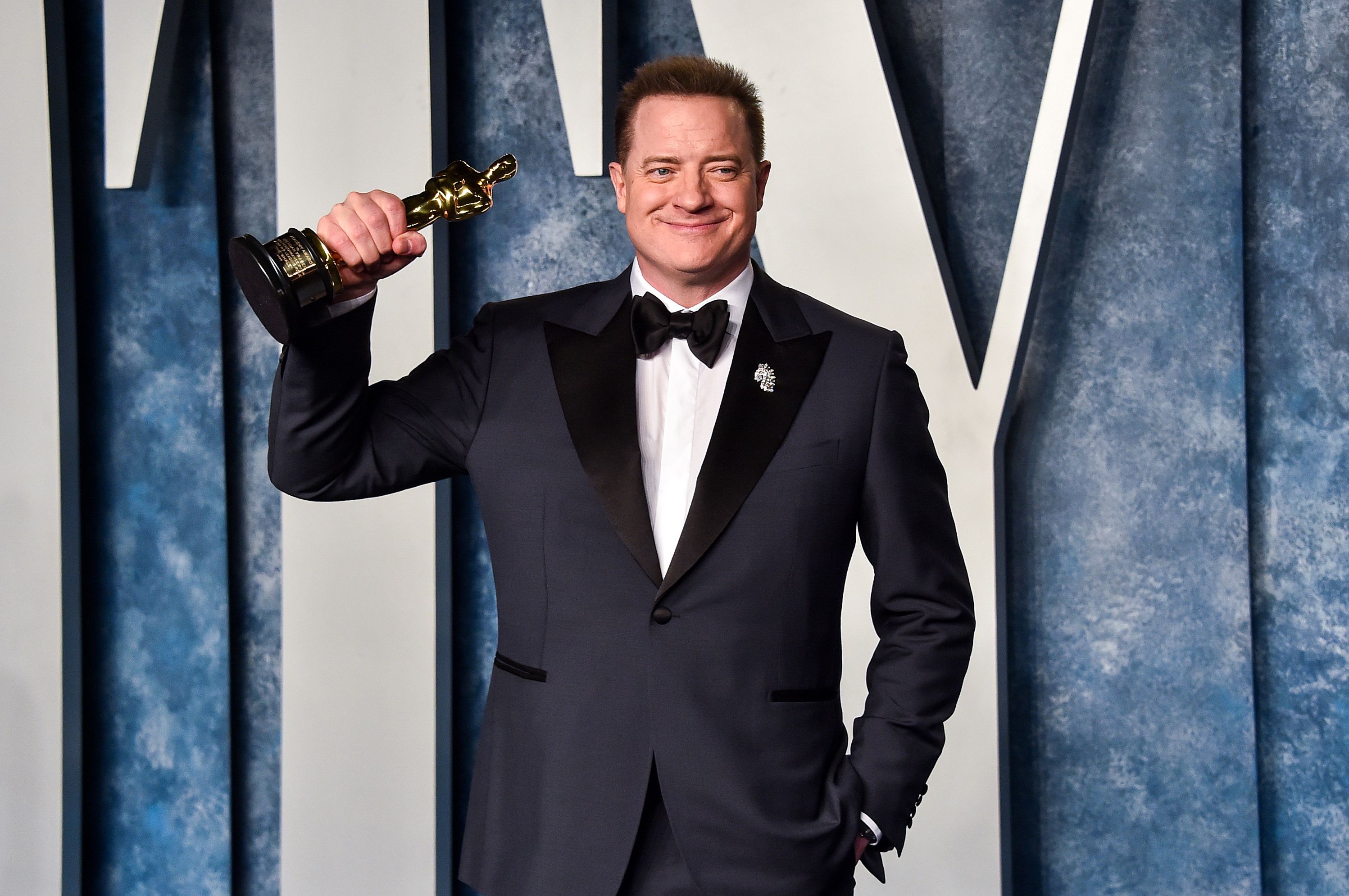 Brendan Fraser in a black suit holding an Academy Award.