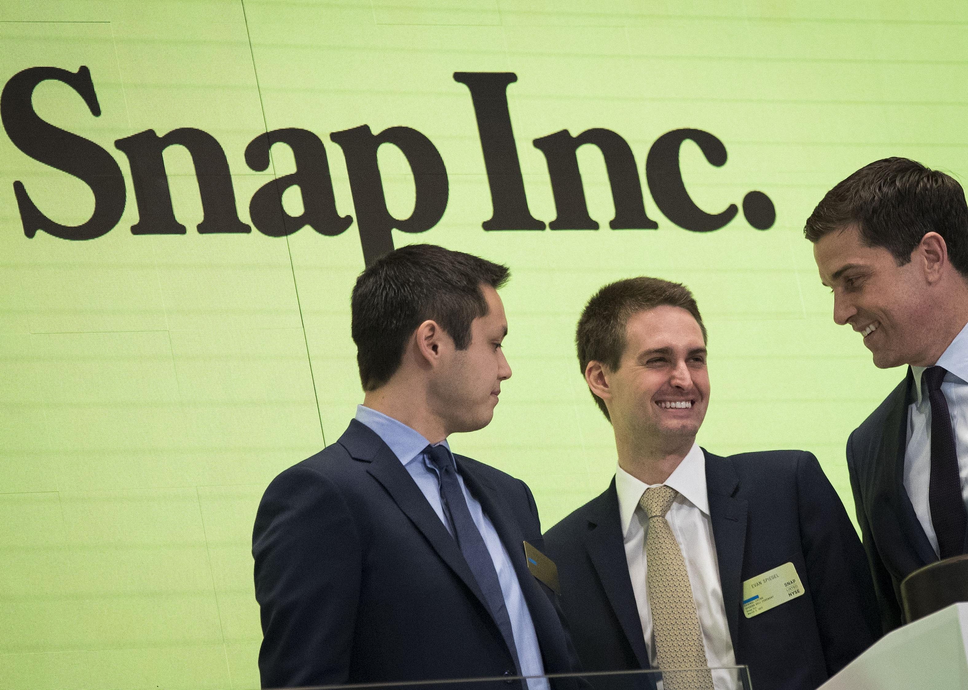 Bobby Murphy and two other men in suits in front of a yellow backgound onstage.