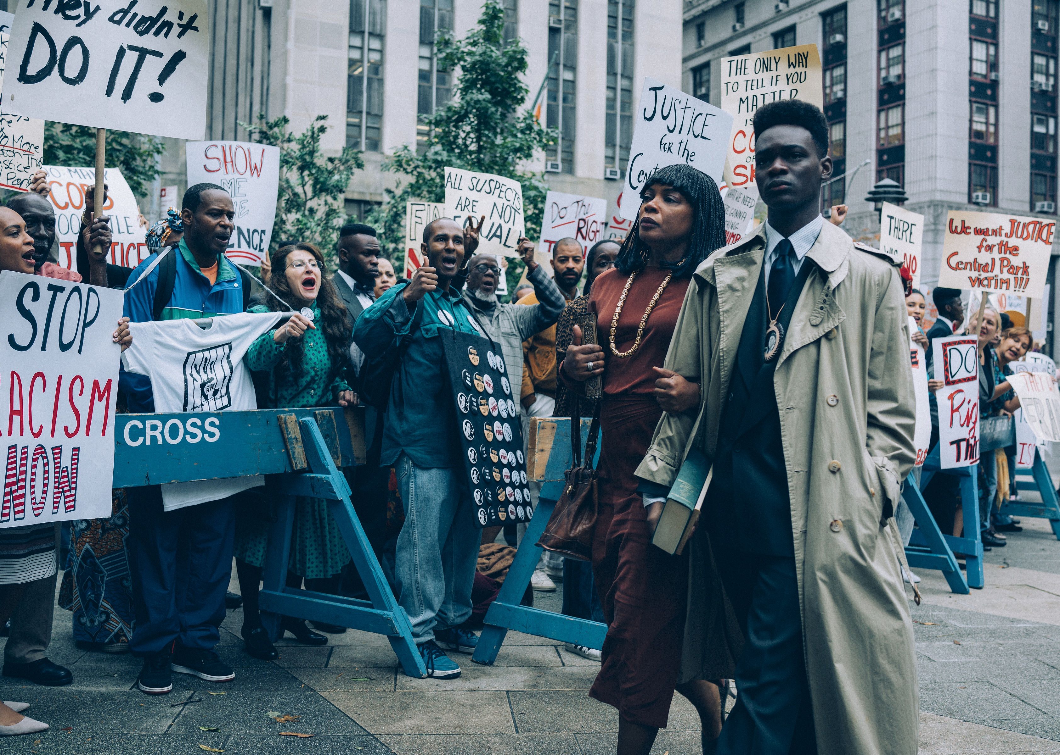 A man and woman walk down a sidewalk lined with protestors.