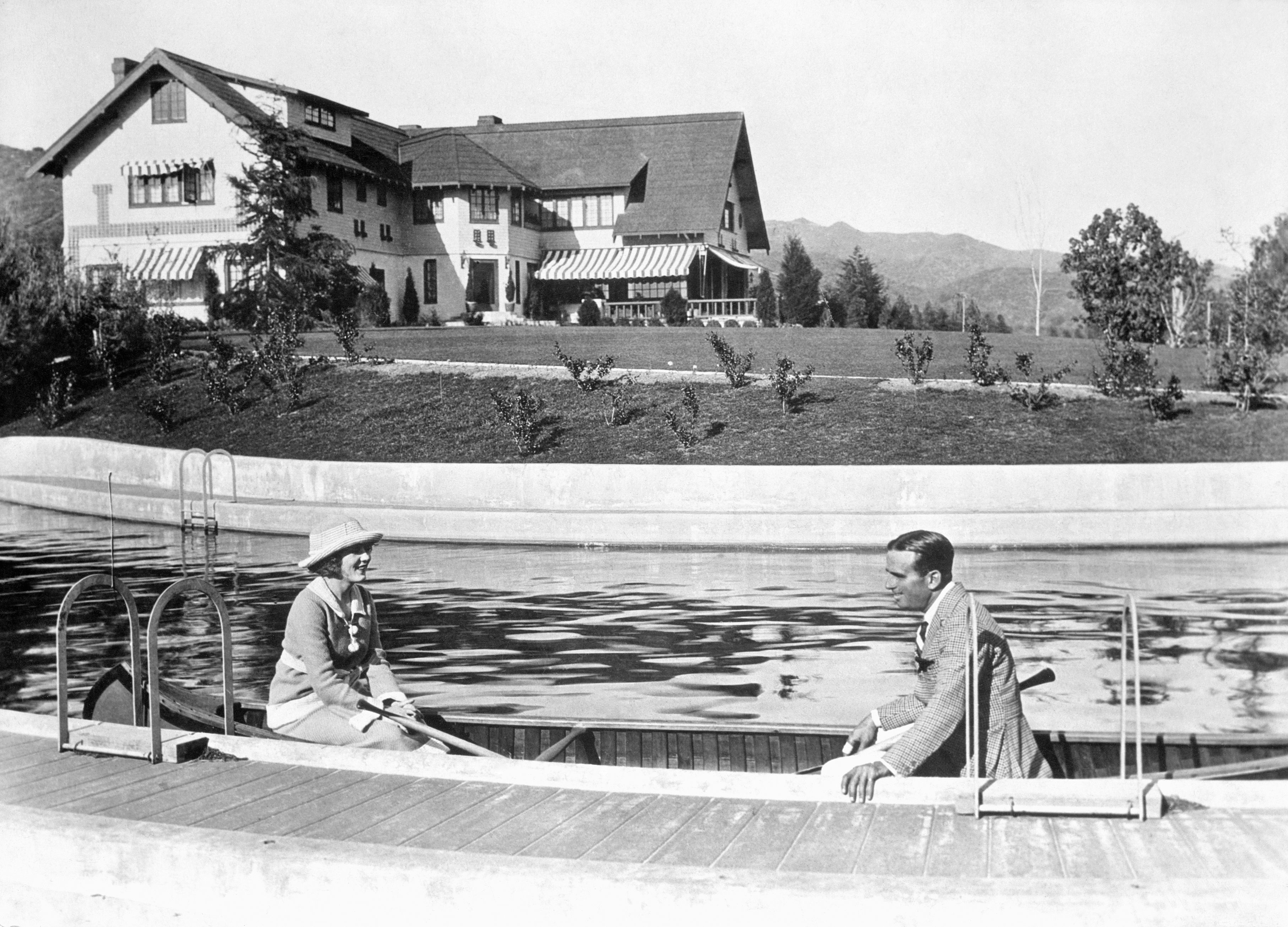 Douglas Fairbanks and Mary Pickford canoe along the swimming pool at their Pickfair estate.