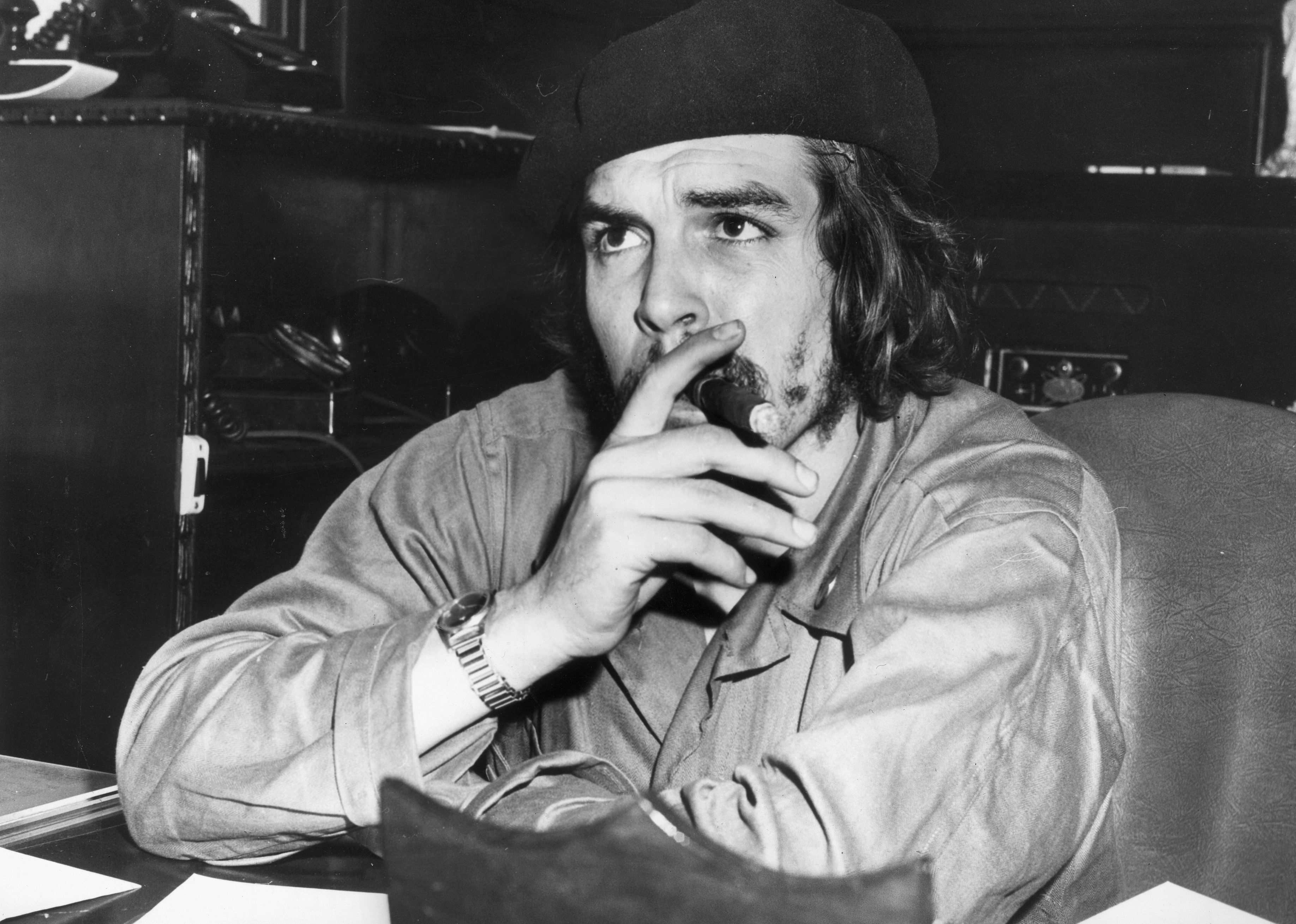 Che Guevara sitting at a desk smoking a cigar.