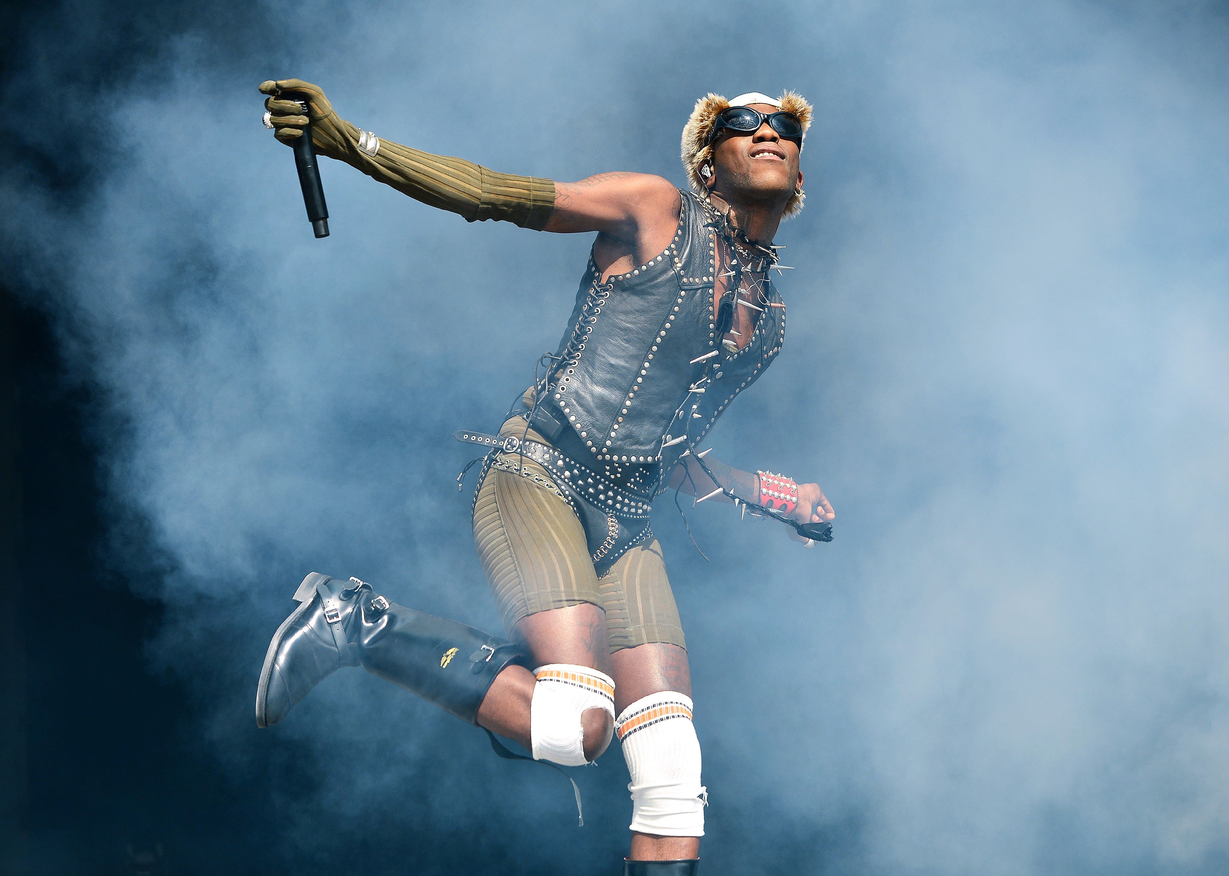 Yves Tumor performing in smoke in a leather vest and boots.