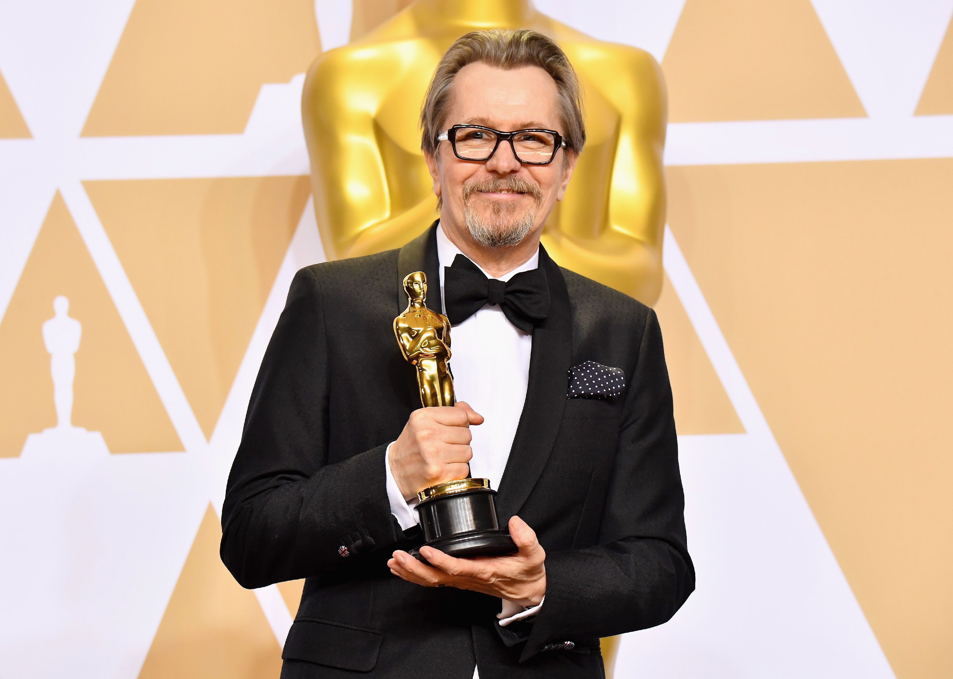 Gary Oldman in a black suit holding an Oscar.