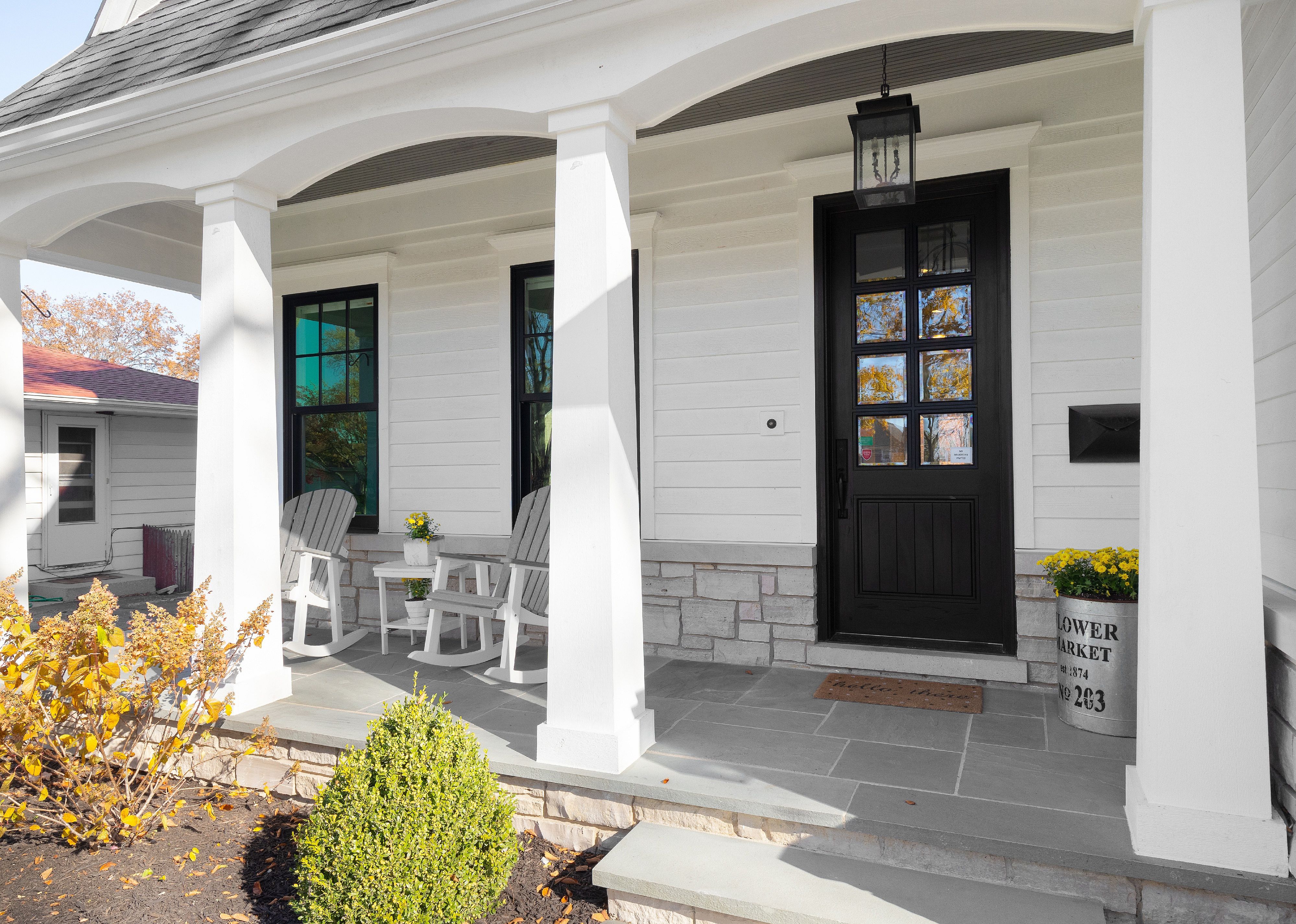 A white house with a black door and rocking chairs on the porch.
